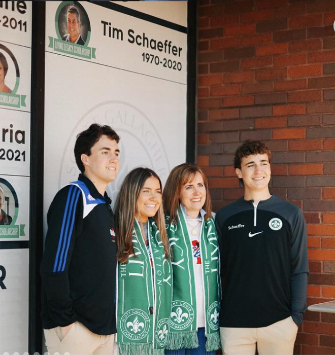 Four people posing indoors in green and black sportswear beside a memorial sign.