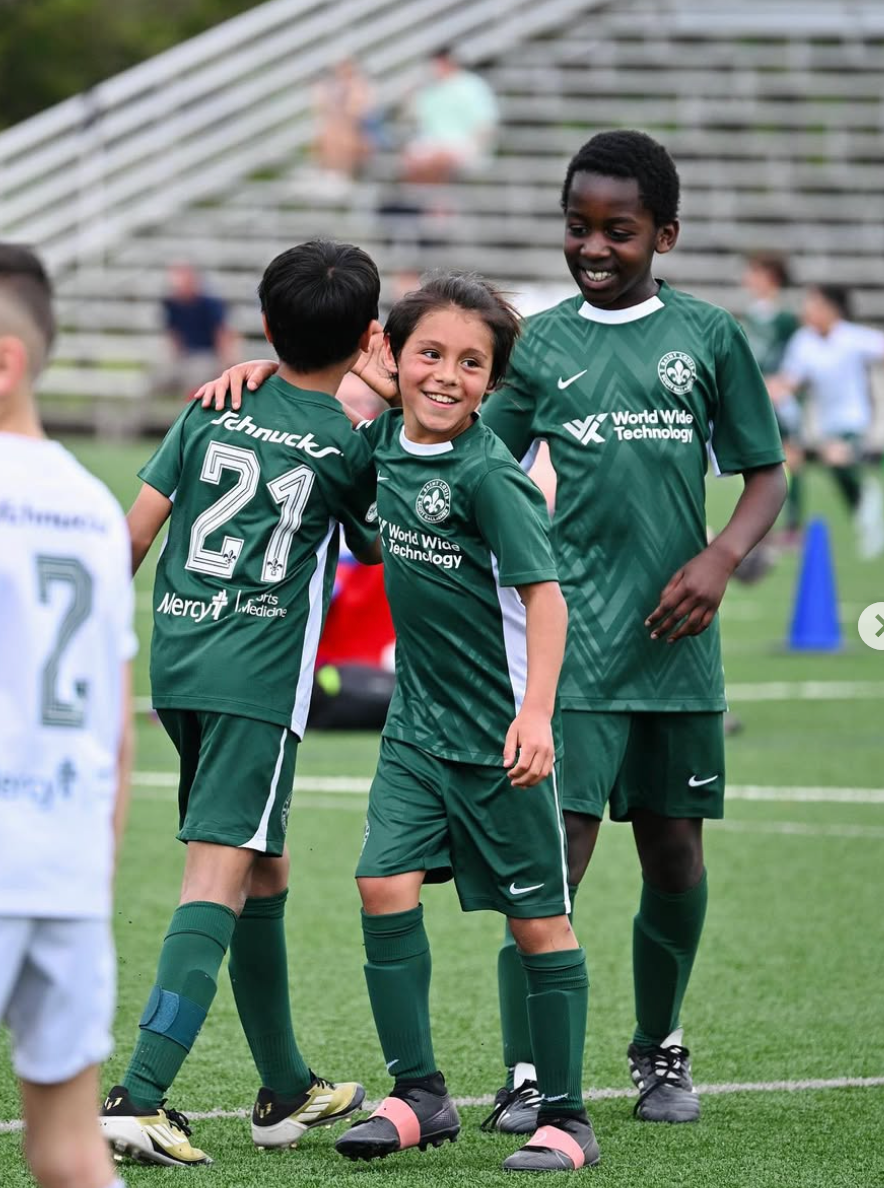 Young soccer players in green uniforms huddle and smile on a field after a game.