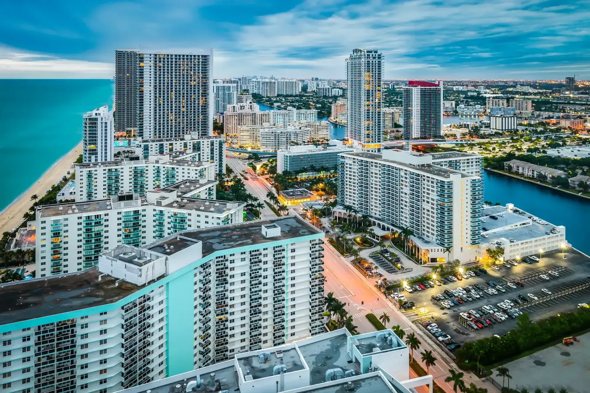Aerial view of a coastal city skyline with high-rise buildings, roads, and turquoise ocean under a blue sky