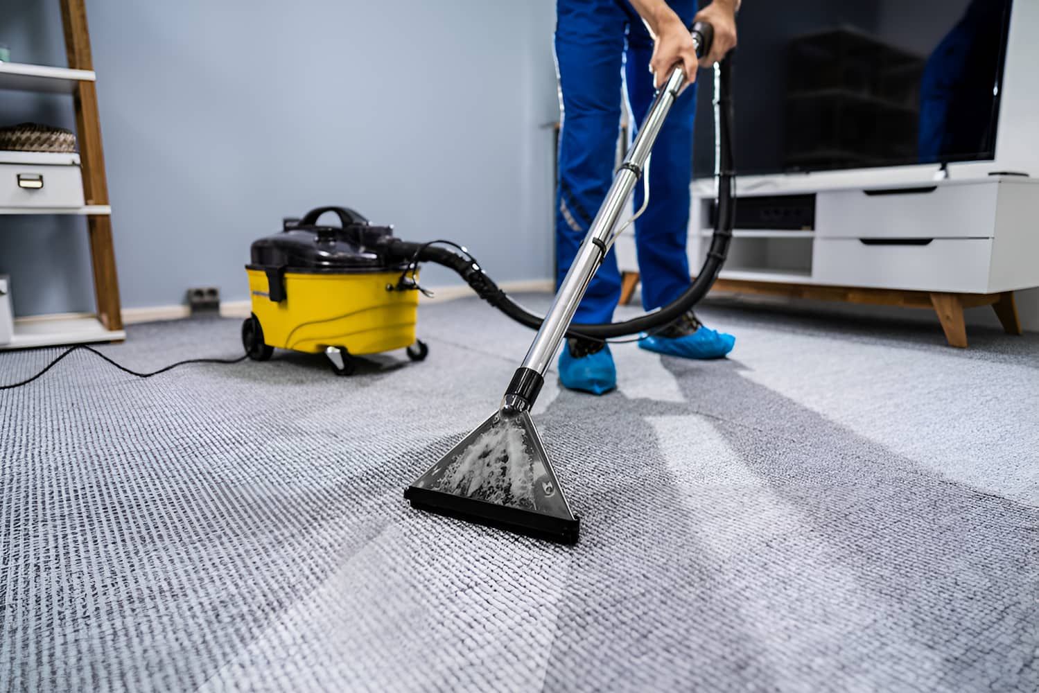 A Person is Using a Vacuum Cleaner to Clean a Carpet in a Living Room — First Choice Cleaning Services in Wodonga, VIC