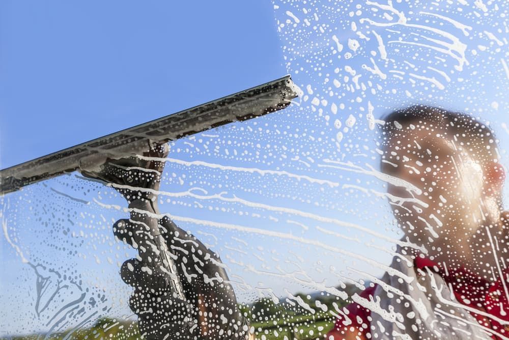 A Man is Cleaning a Window With a Squeegee — First Choice Cleaning Services in Wangaratta, VIC