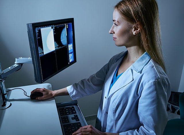 Woman smiling during a mammogram; healthcare worker assists.