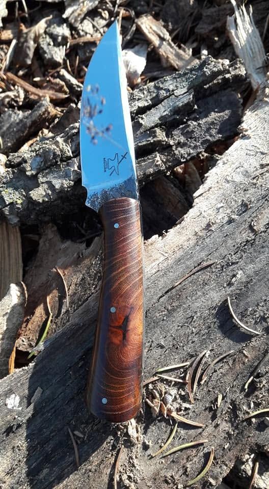 Blue-bladed knife with a brown handle lying on charred debris and wood ash
