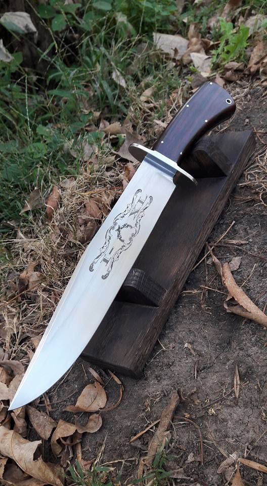 Large knife with white blade and black handle resting on a log outdoors among leaves and grass