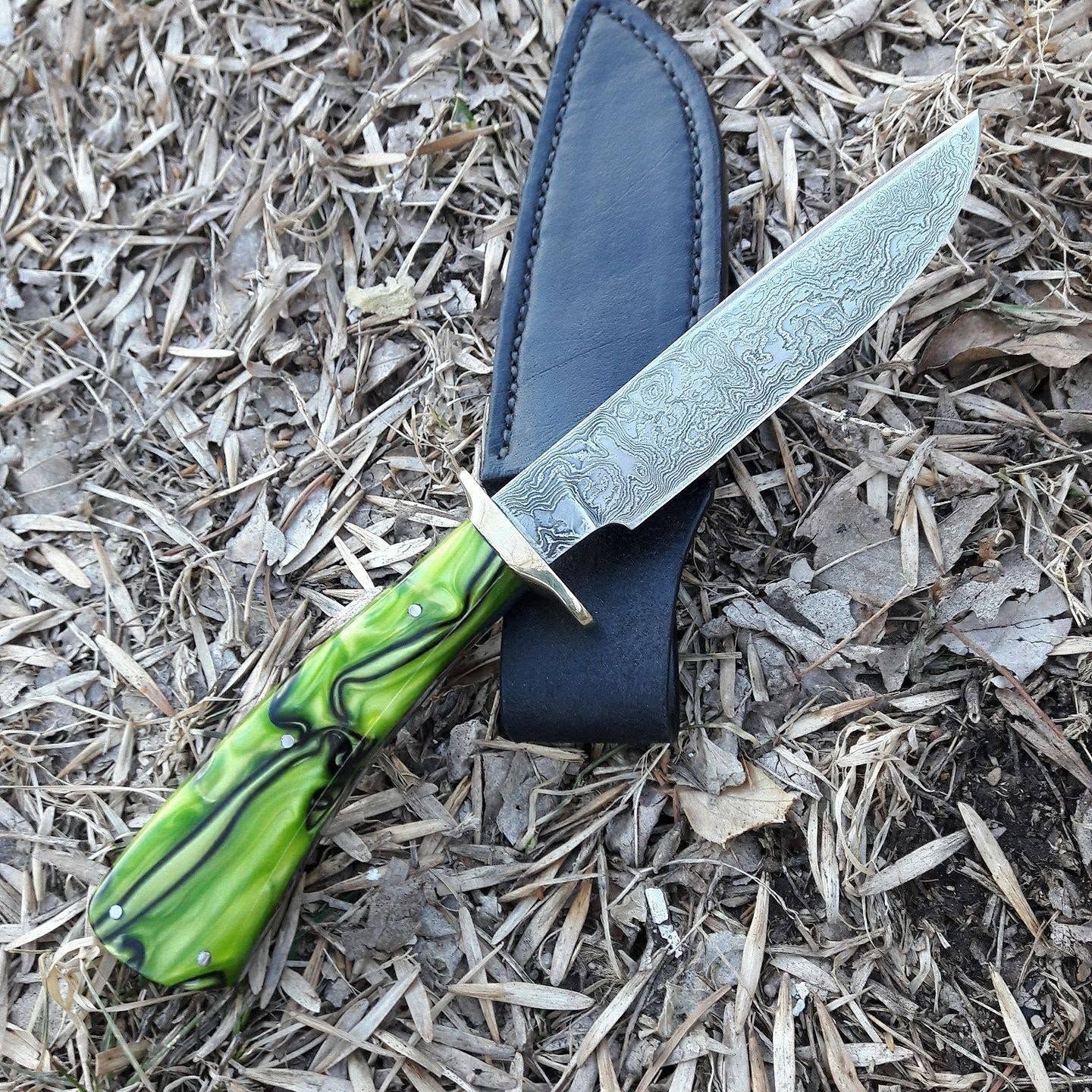 Decorative dagger with green handle and textured silver blade resting on a black sheath over wood chips