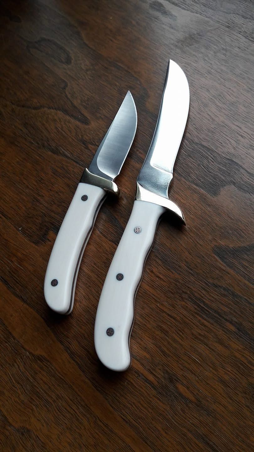 Two kitchen knives with white handles on a dark wooden surface