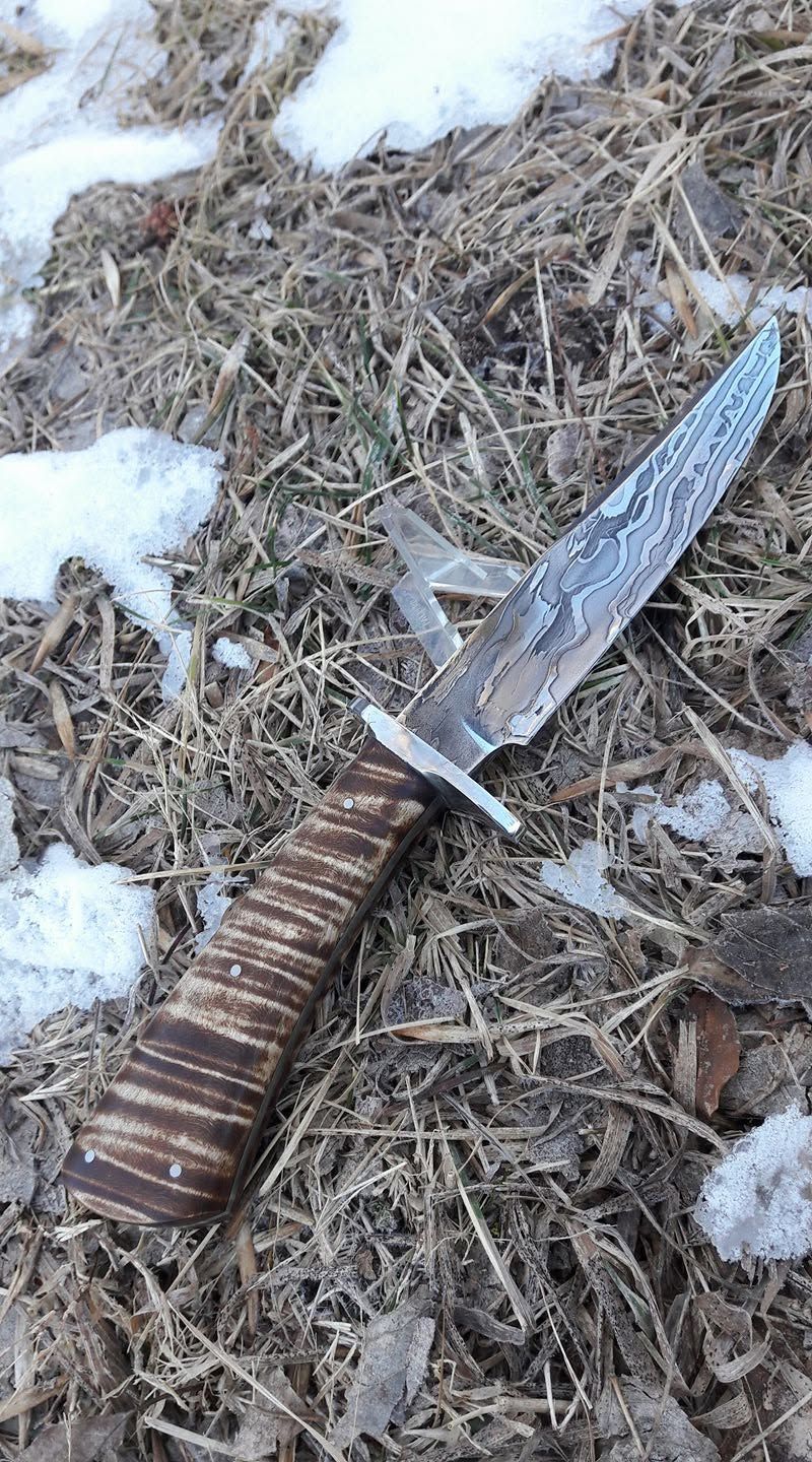 Large knife with a worn brown handle lying on dried grass with patches of snow