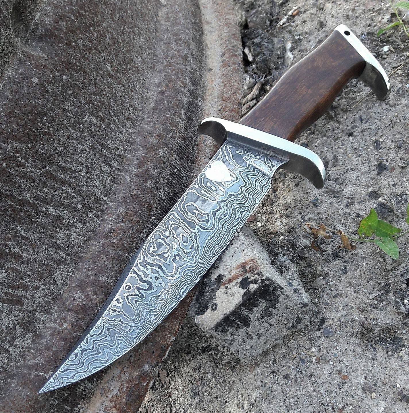 Damascus-style fixed-blade hunting knife with wood handle resting on a rock