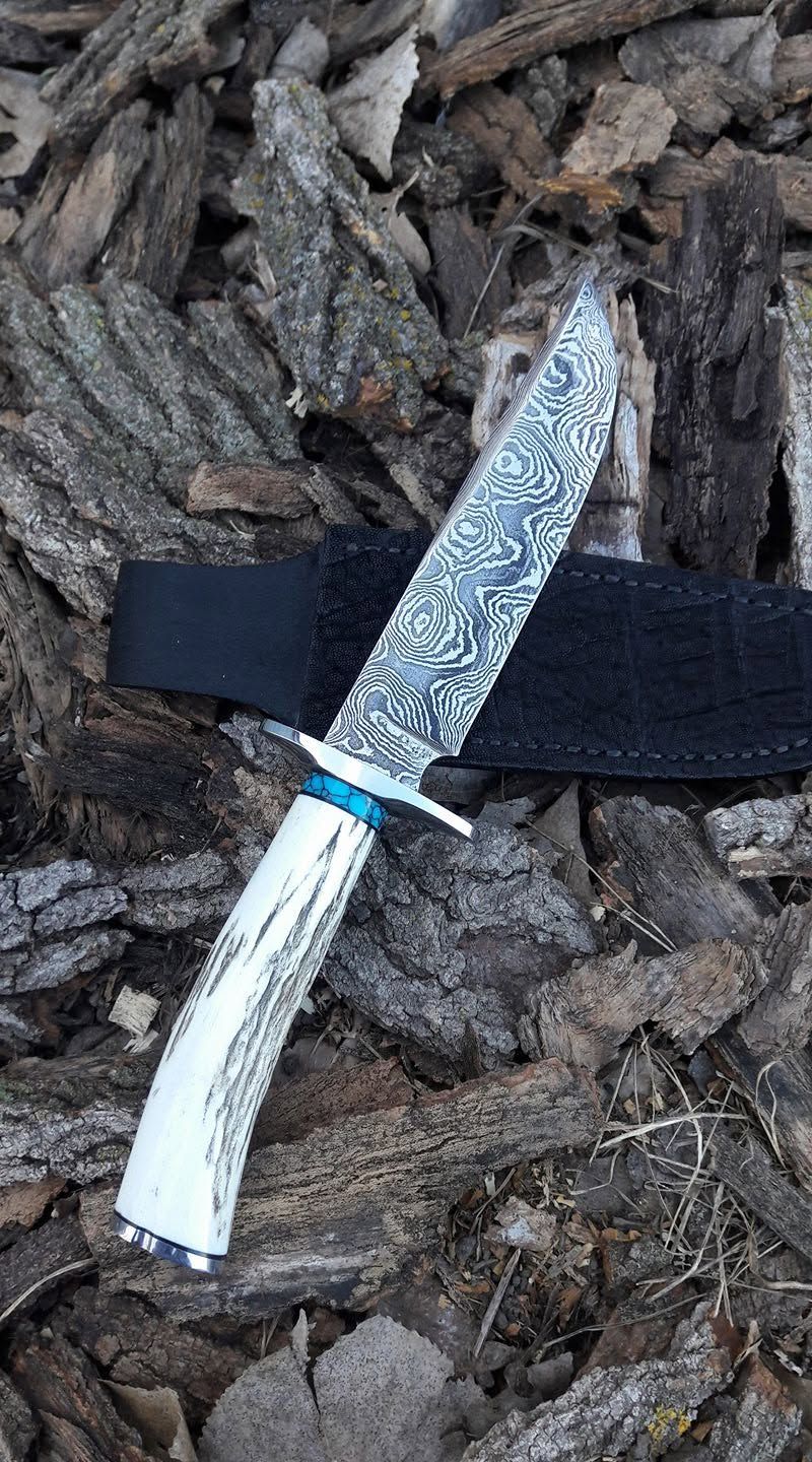 Decorative knife with white handle lying on bark mulch beside a black strap