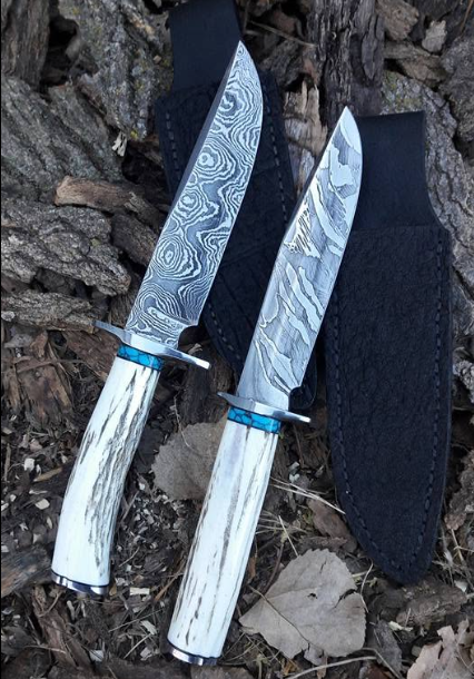 Two engraved knives with white handles resting on bark mulch beside a black sheath