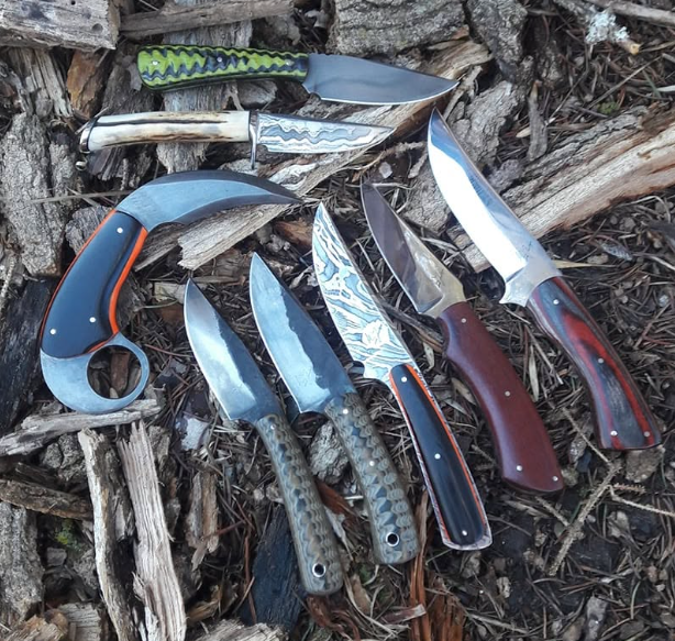 Six knives of varying sizes with colored handles laid on tree bark and wood in an outdoor setting