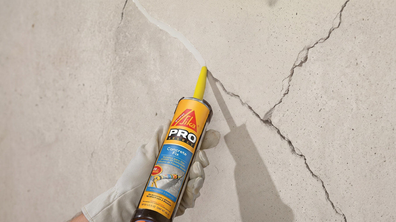 Caulking gun with yellow nozzle applying sealant to a cracked wall surface.