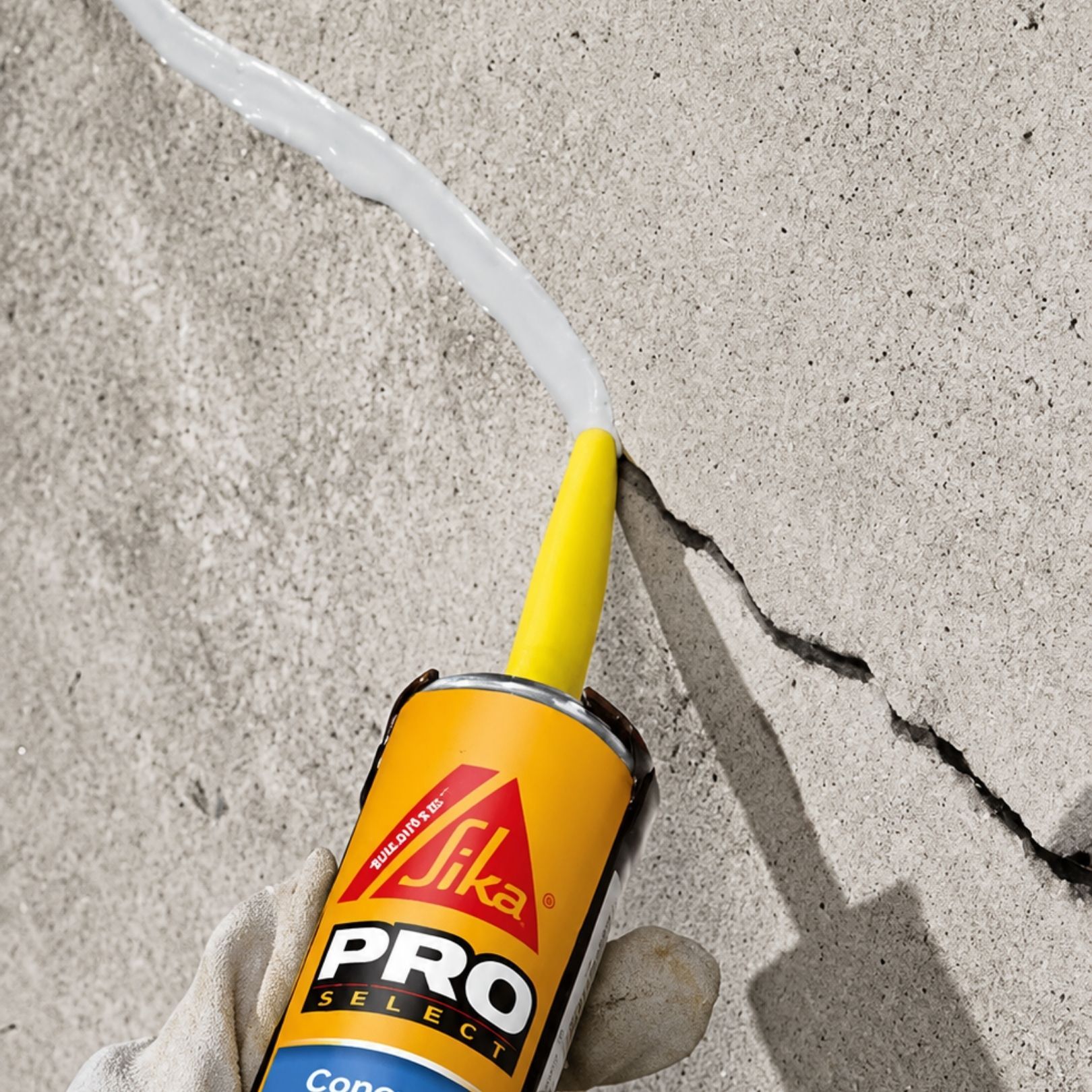 Gloved hand holding Sika PRO sealant tube near a crack in a concrete wall