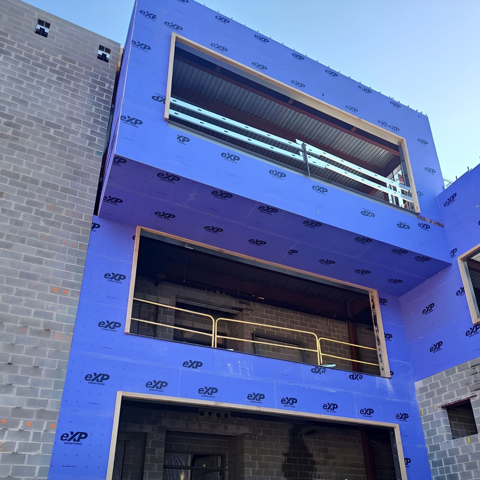 Blue building facade under construction with exposed brick sides and open window openings.
