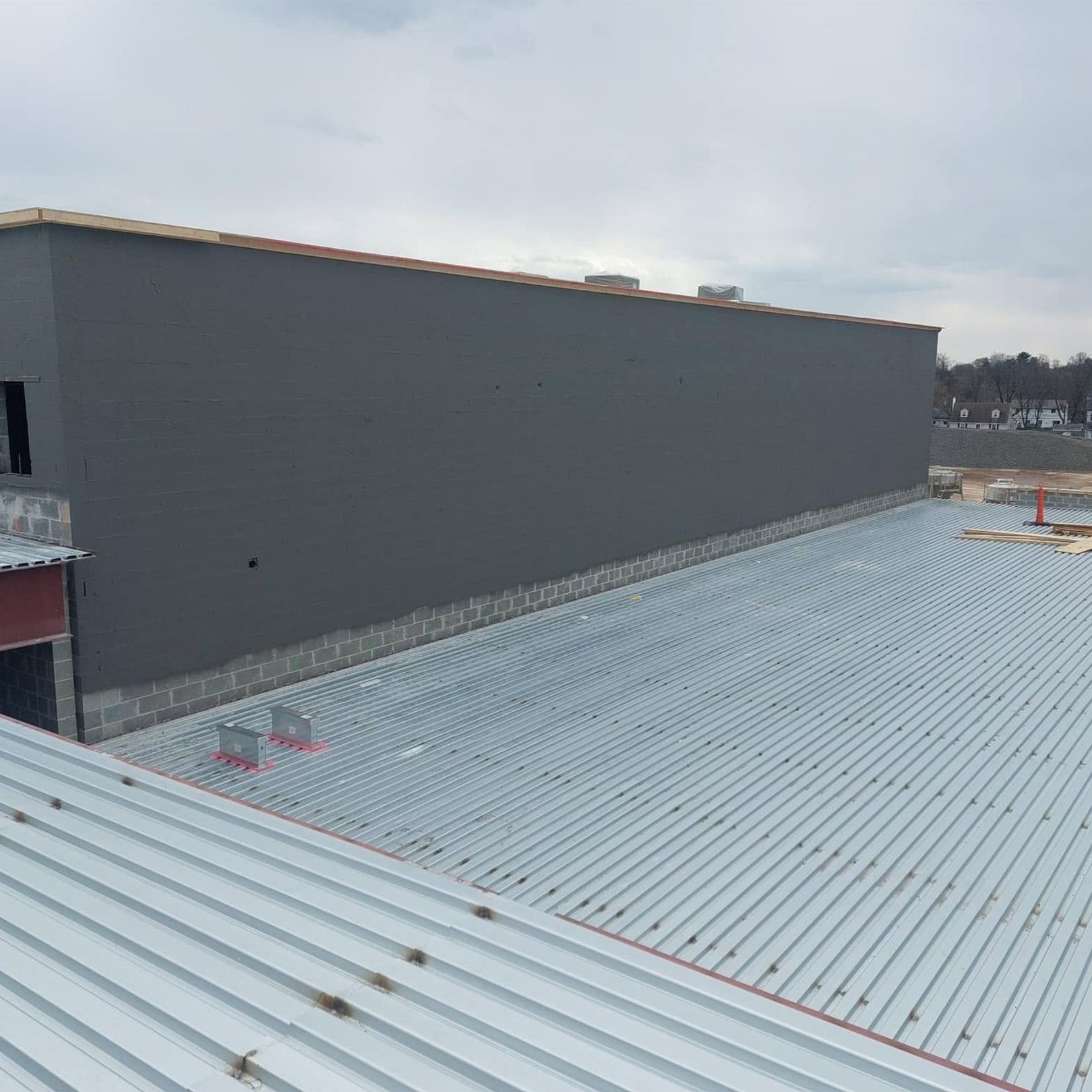 Rooftop with light gray corrugated metal, a tall gray wall, and a cloudy sky above.