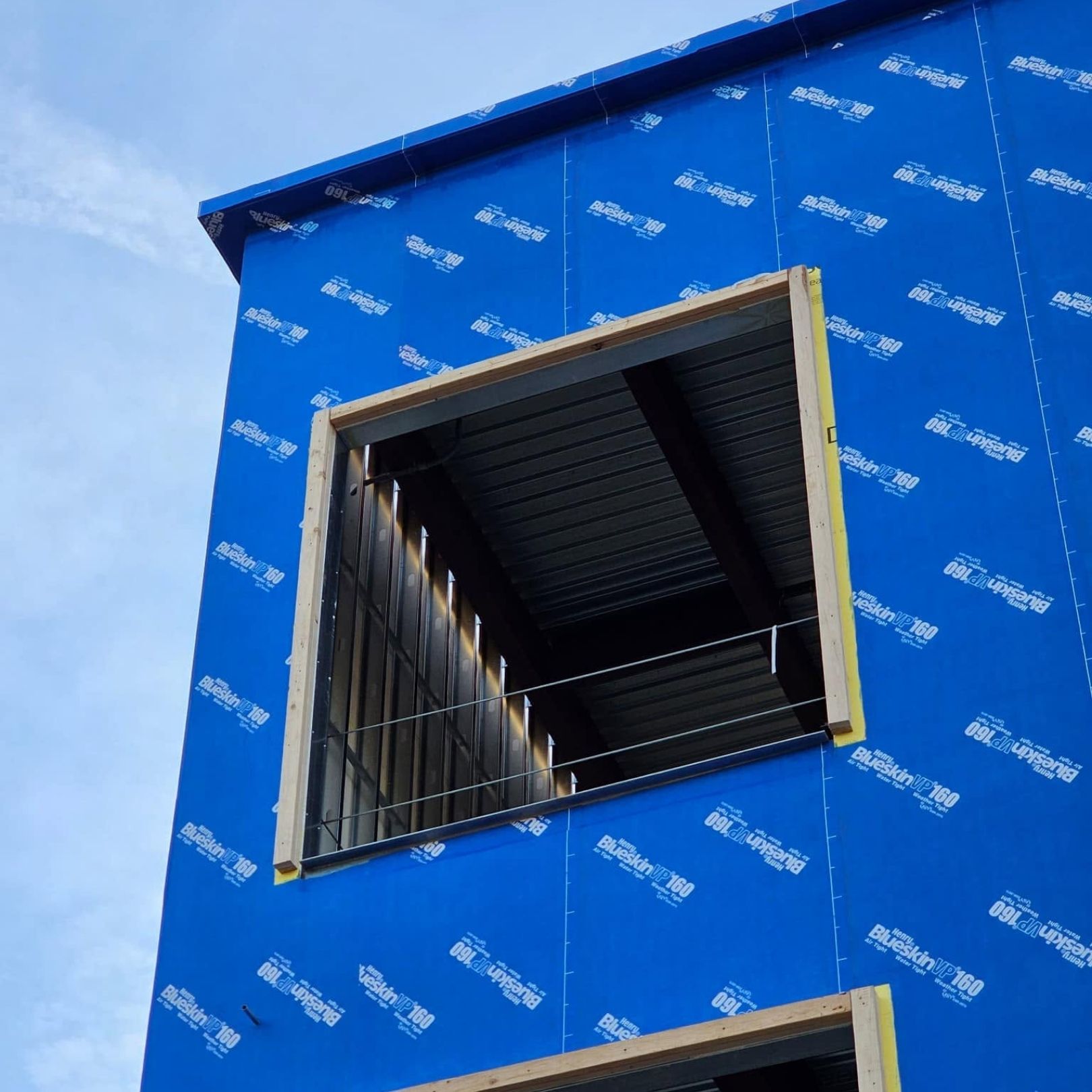 Blue building exterior with a square window opening and metal bars against a cloudy sky