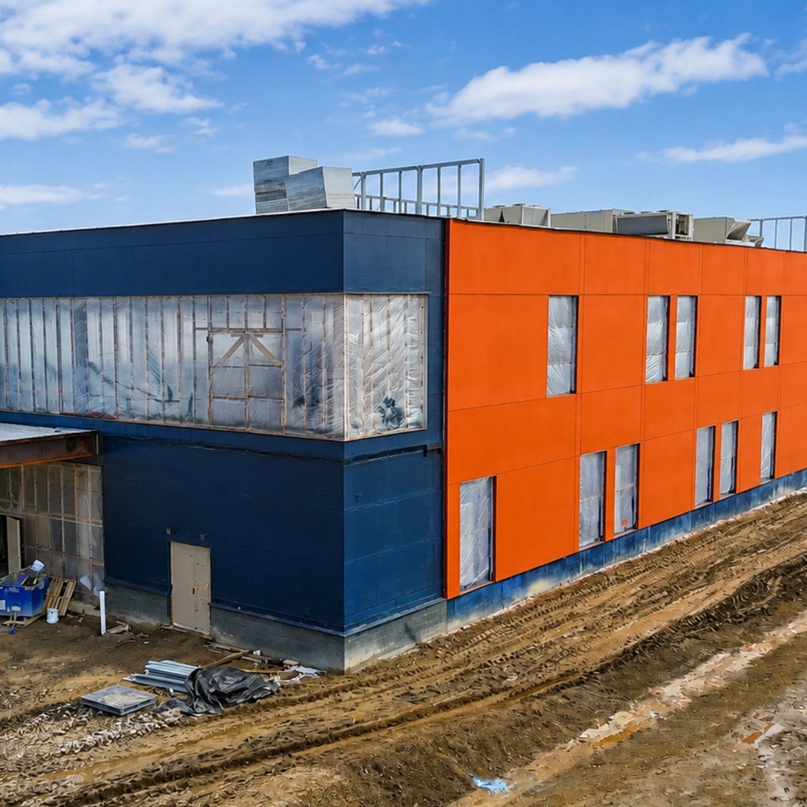 Blue and orange building under construction beside a muddy dirt road