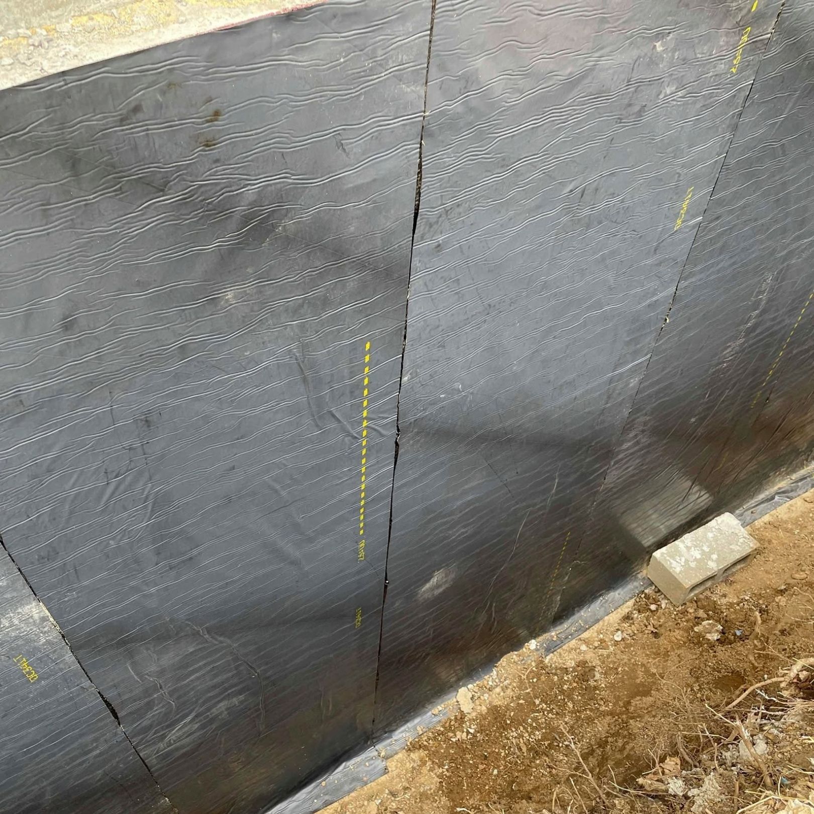 Black mesh barrier along a dirt edge, with a vertical seam and a small concrete block at the base.