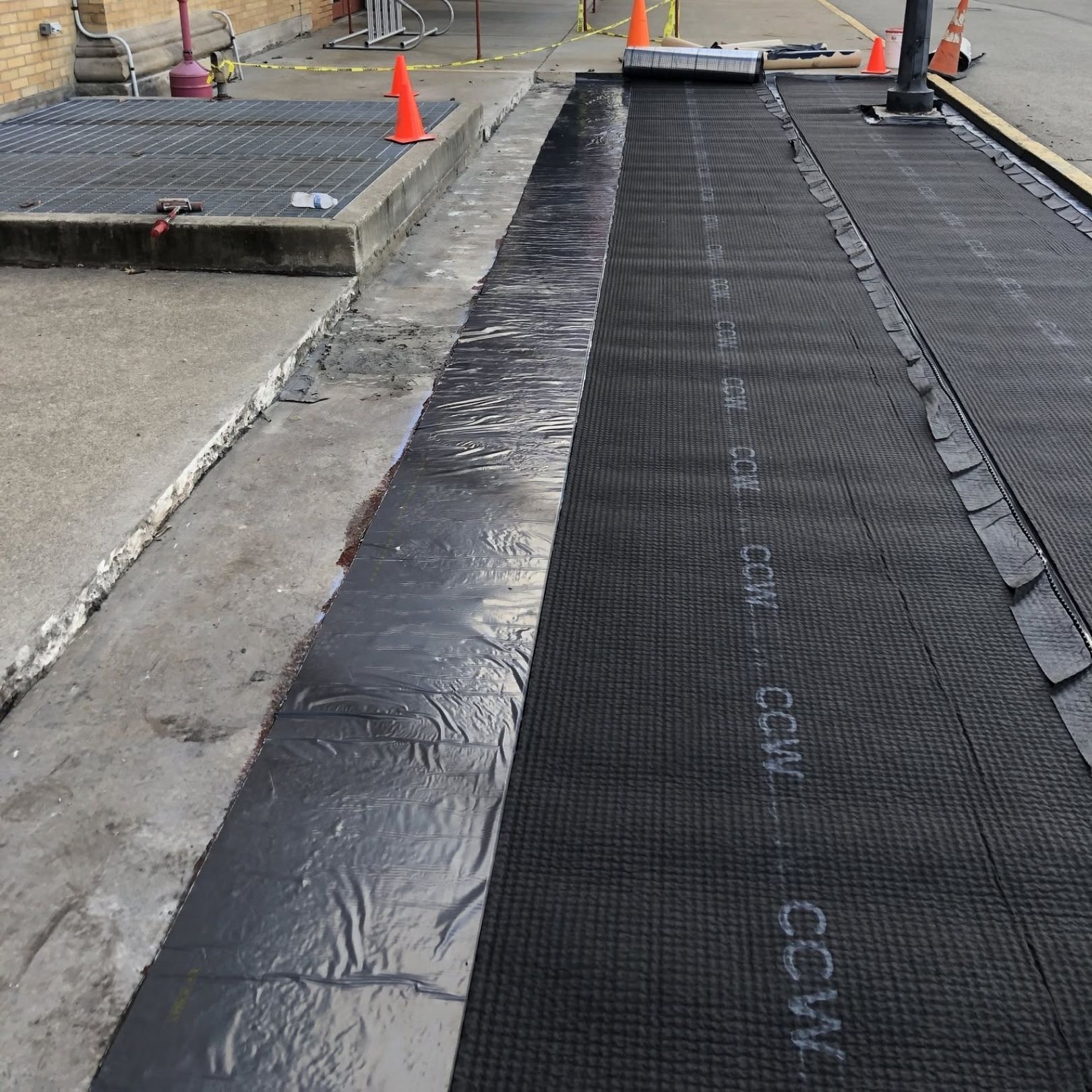 Construction walkway with black matting beside a concrete curb and orange traffic cones.