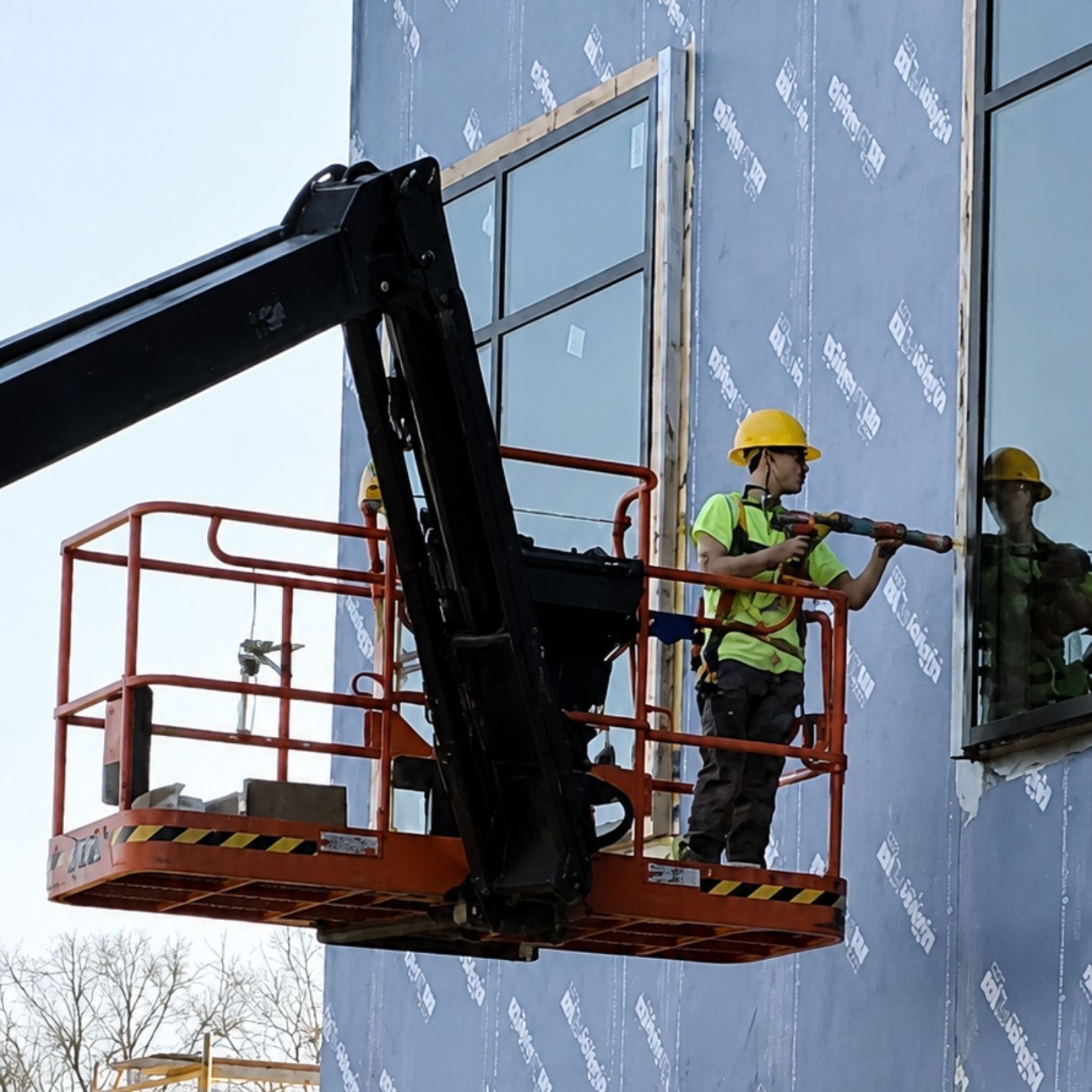 Two workers in hard hats on a lift painting a building exterior