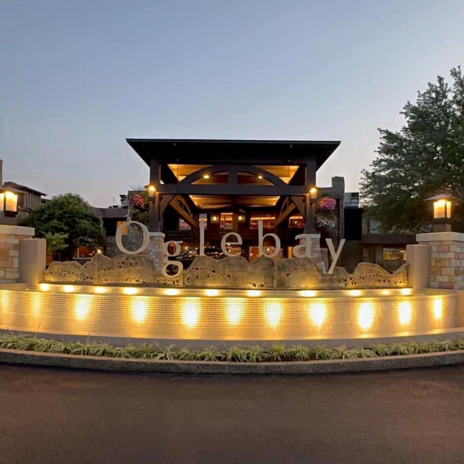 Illuminated modern stone entrance sign at dusk with warm lights and landscaped greenery