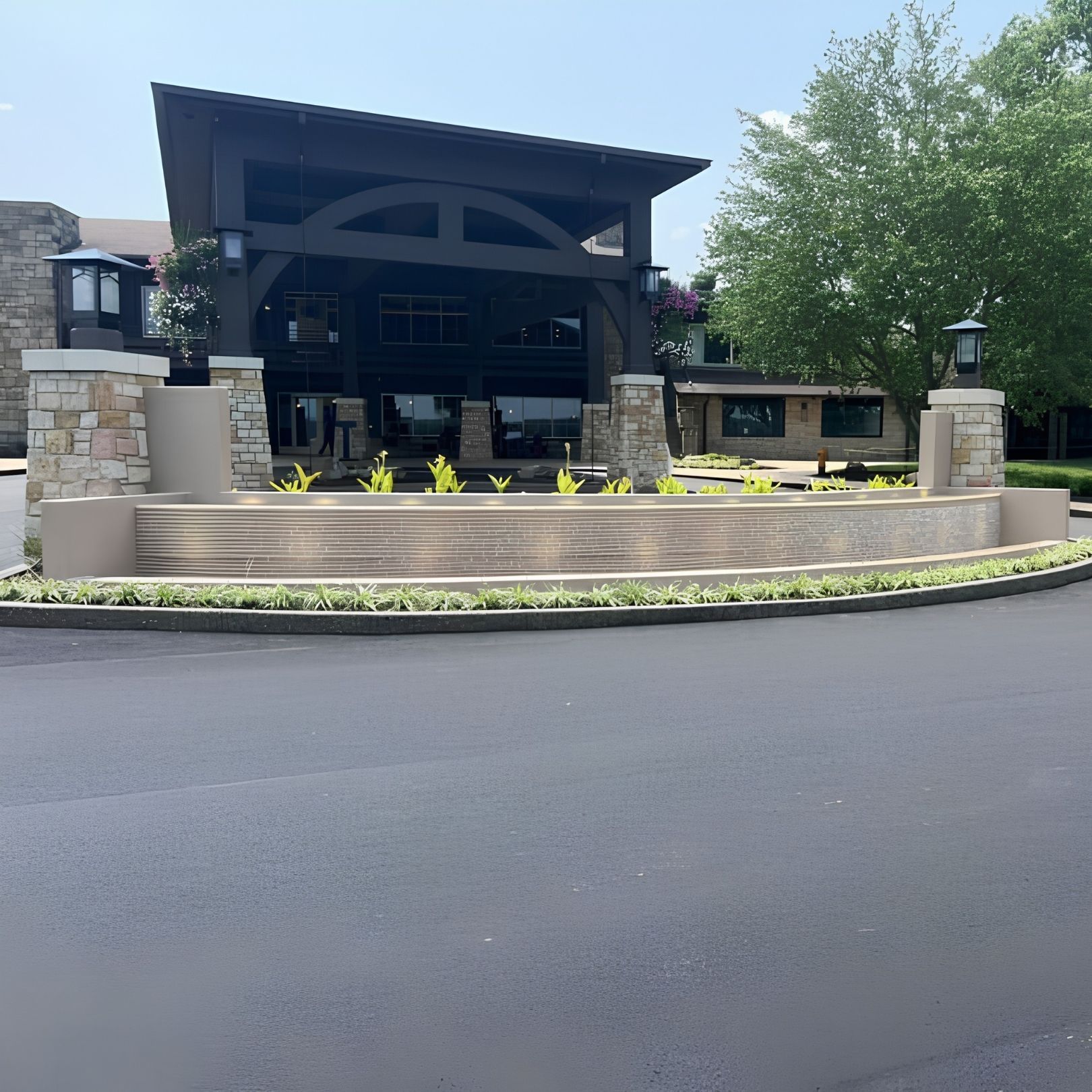 Modern building with stone pillars and landscaped entry beside a paved road
