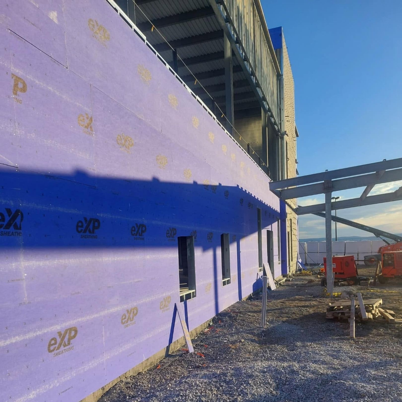 Purple construction site exterior with exposed framing, windows, and gravel ground under blue sky