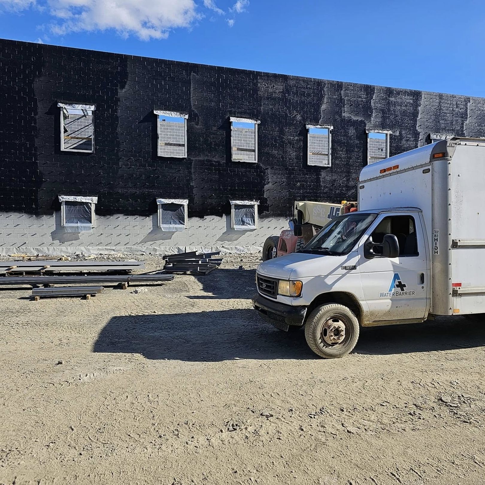 Worker truck parked outside a black building under construction on a sunny day