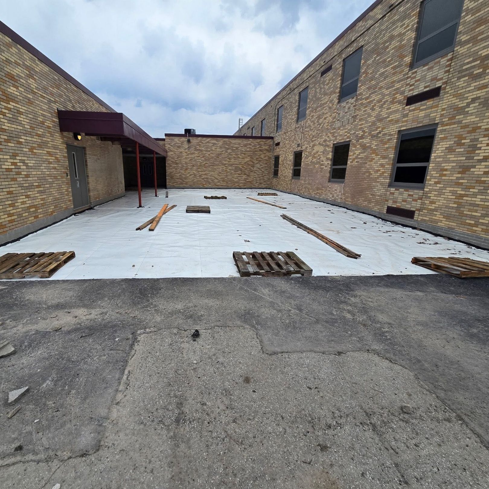 Brick alley with a newly poured white concrete slab between two buildings under a cloudy sky