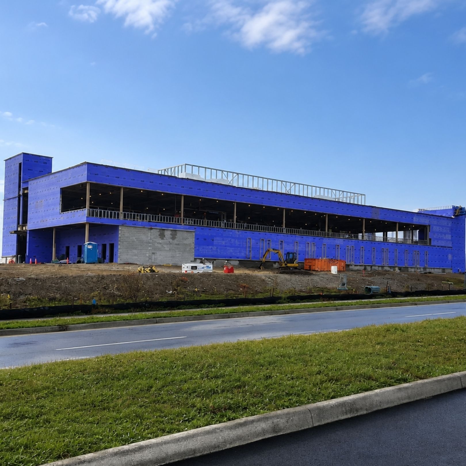 Blue industrial building under construction beside a road and grassy verge