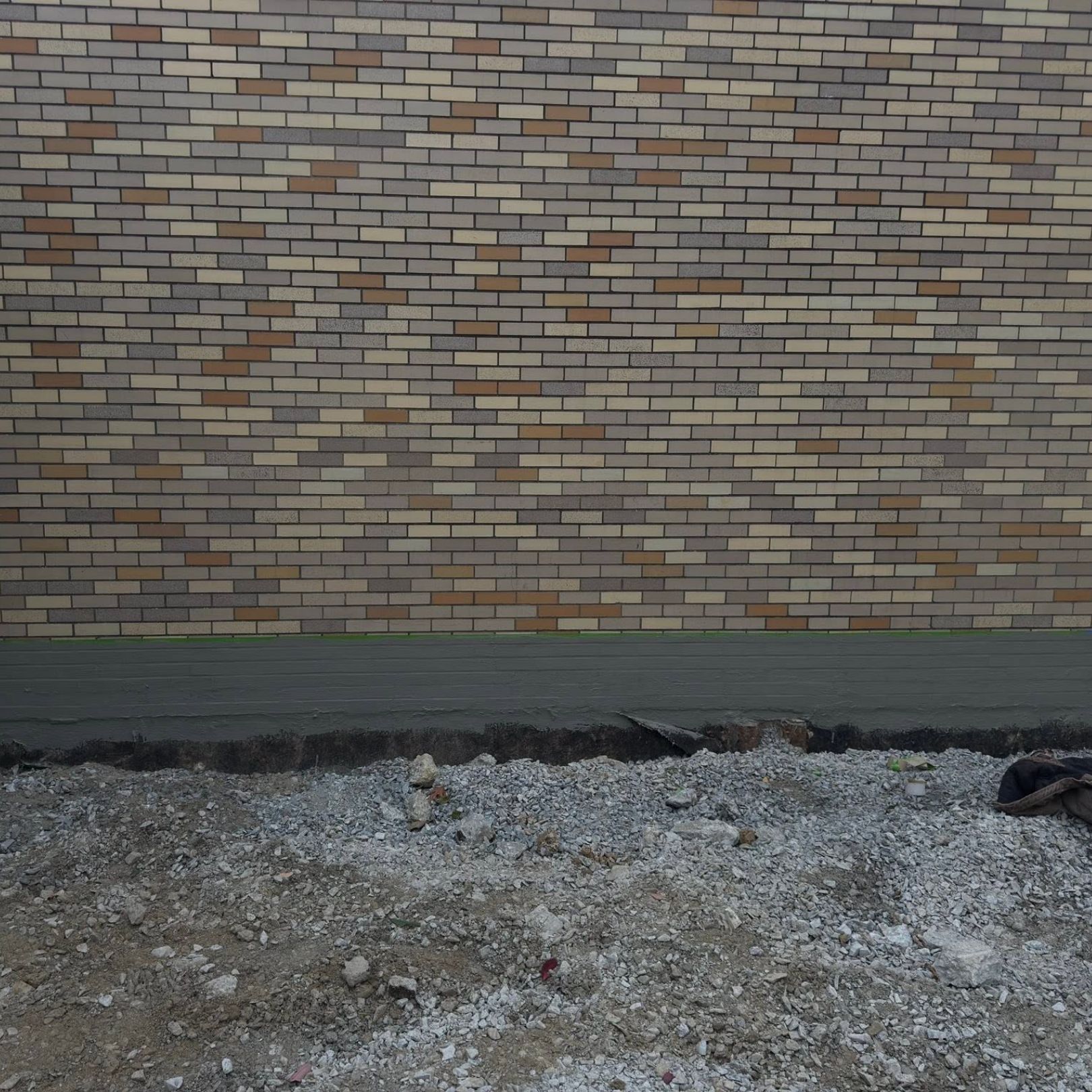 Brick wall behind a cracked concrete curb and gravel ground under overcast light