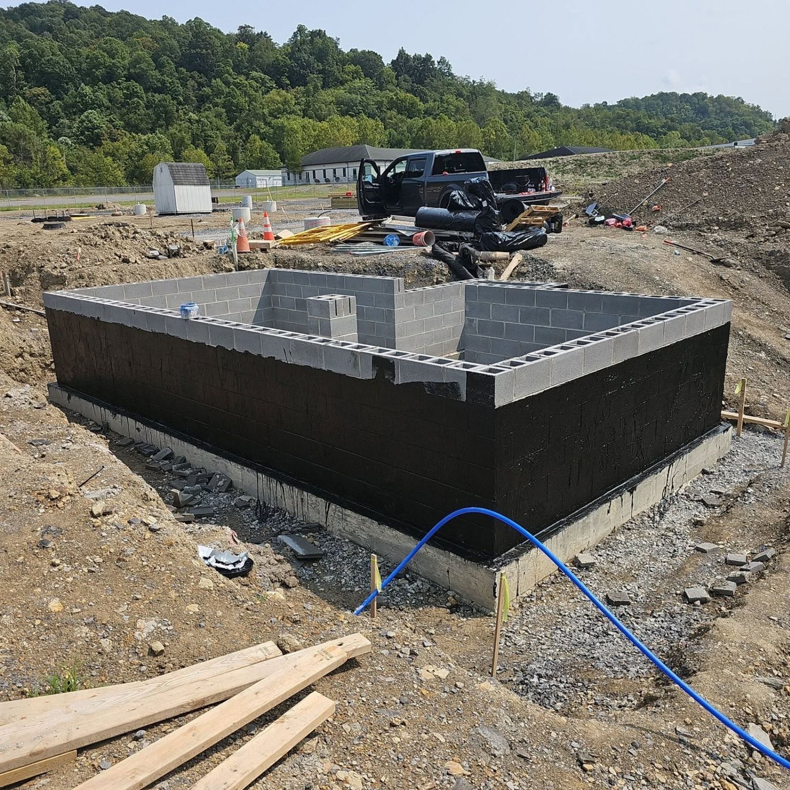 Construction site with a black rectangular concrete tank and a pickup truck in the background
