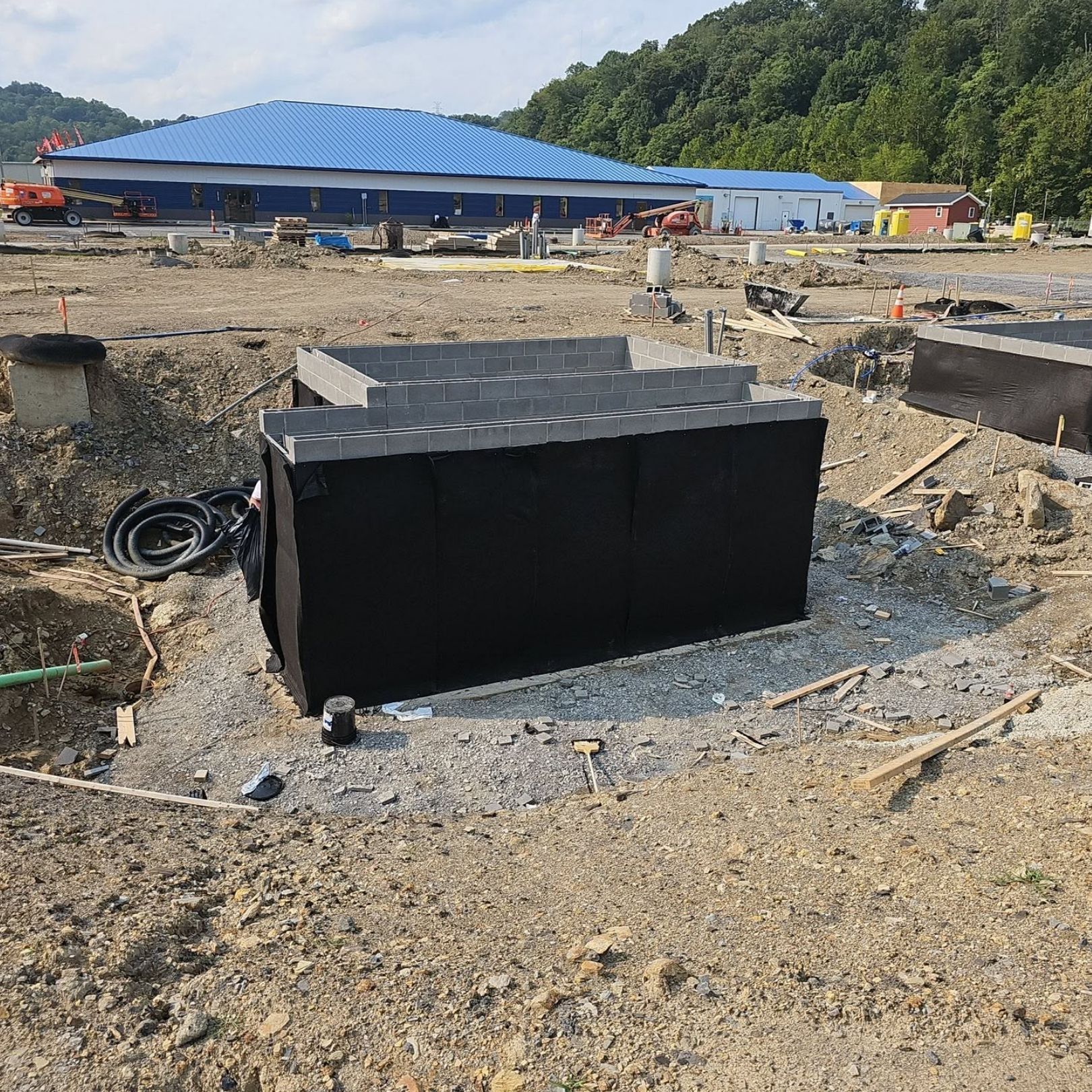 Black rectangular tank in a gravel construction site with blue-roofed buildings in the background