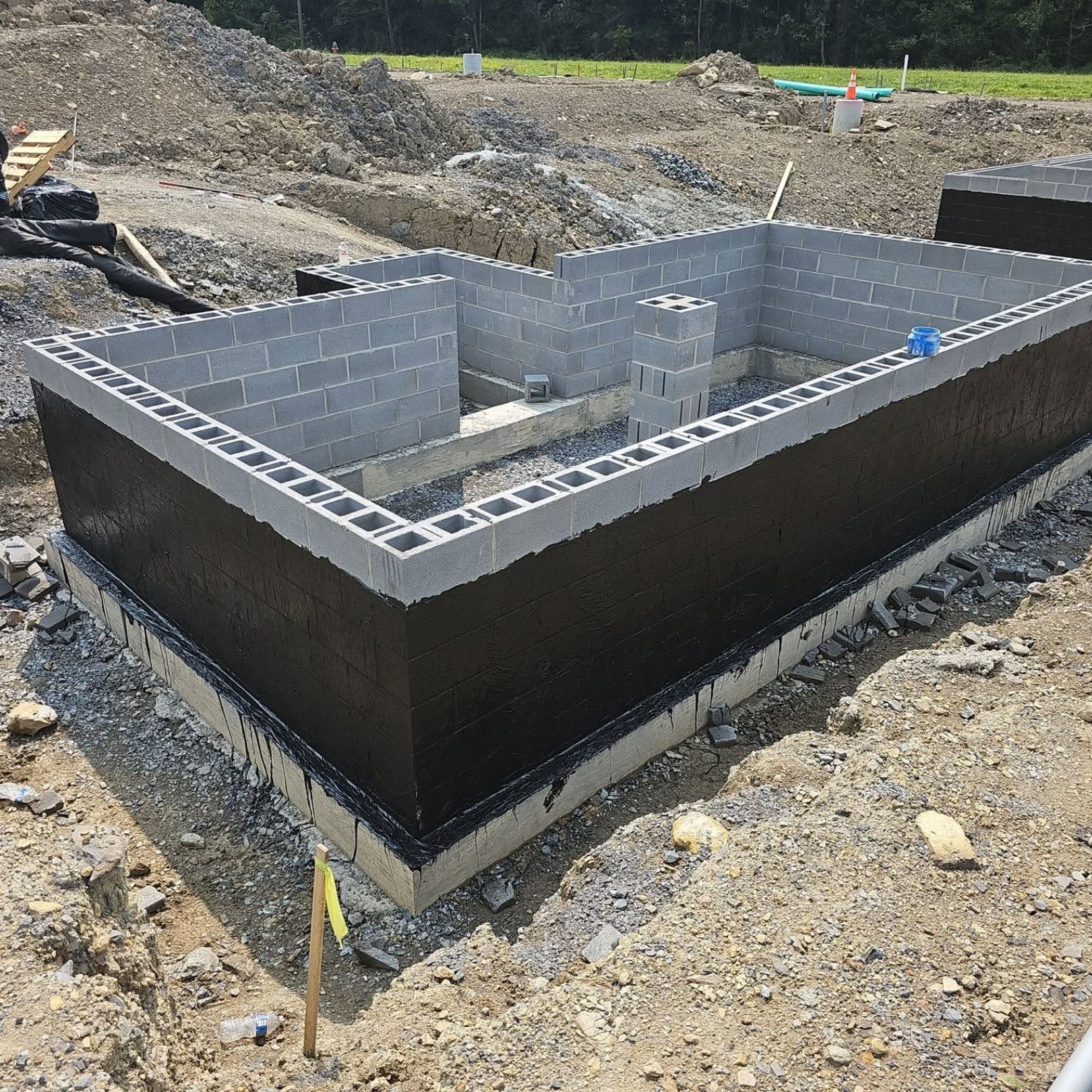 Concrete block foundation under construction with black waterproofing and gravel surrounding it