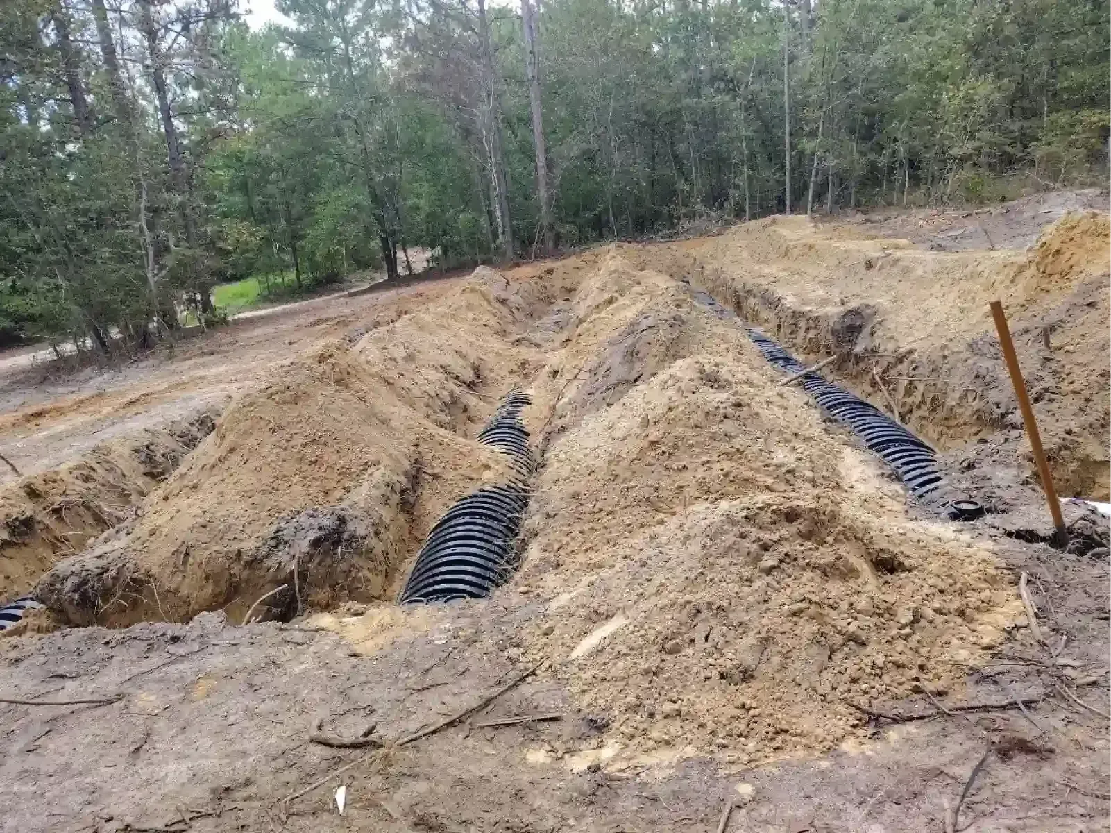 Black plastic septic drain field chambers installed in open trenches in a wooded area.