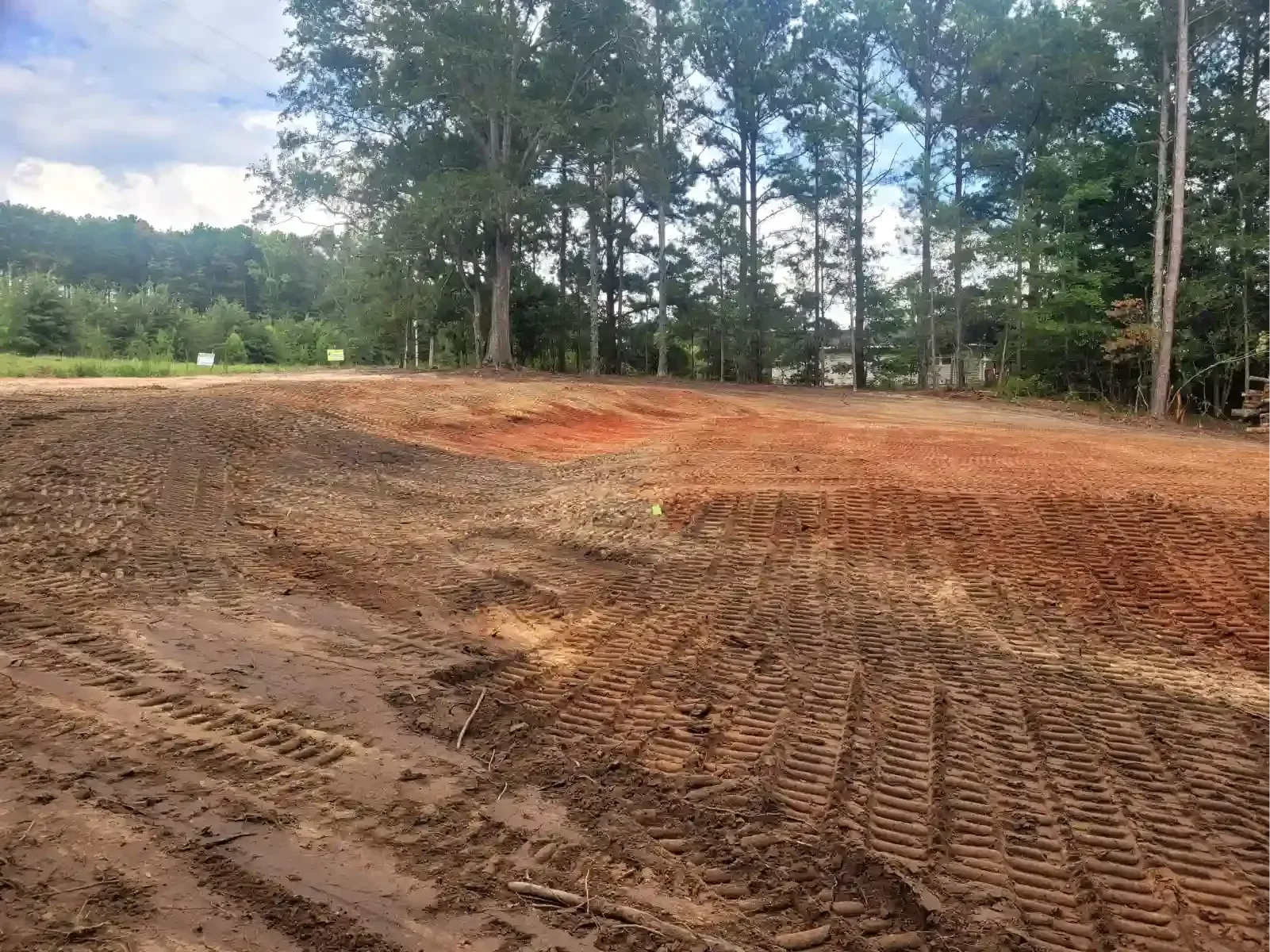 A yellow bulldozer levels a dusty, dirt field under a cloudy blue sky.