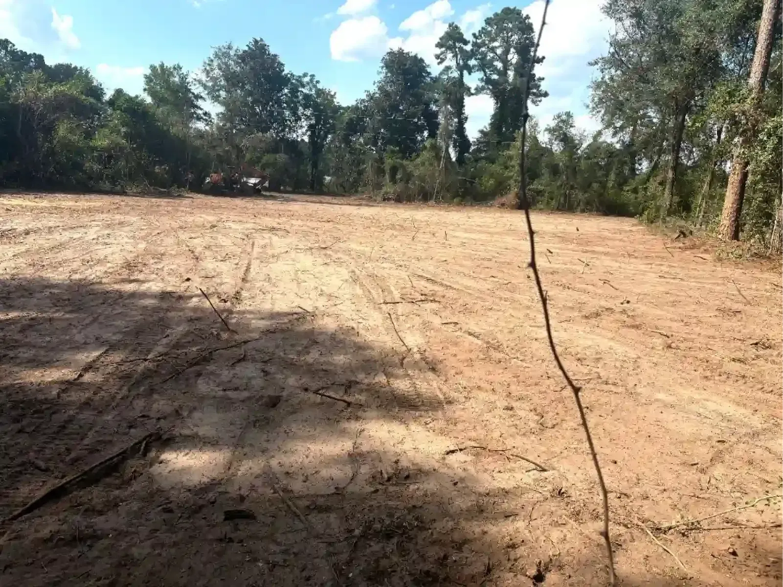 A yellow bulldozer levels a dusty, dirt field under a cloudy blue sky.