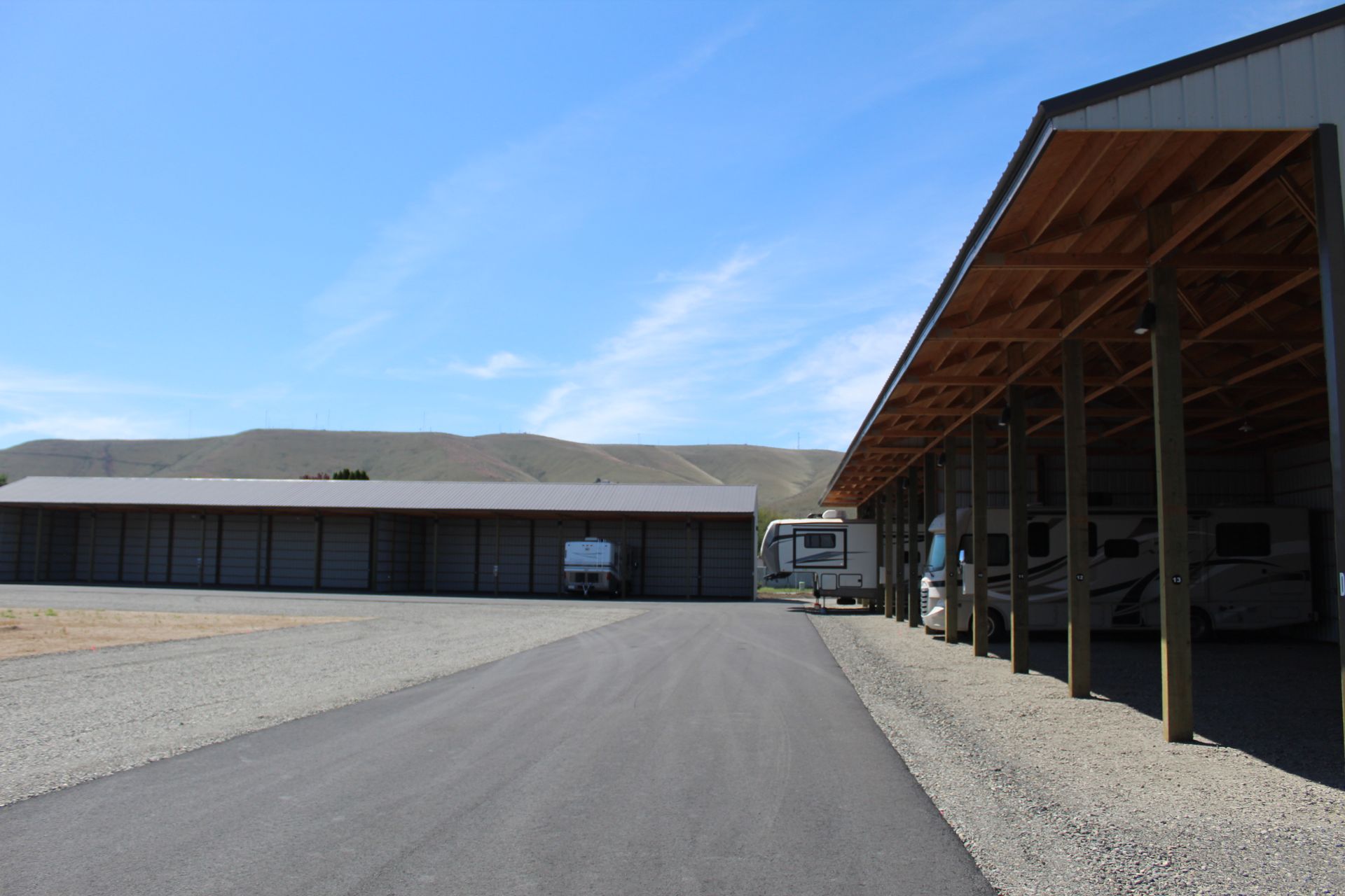 Industrial warehouse building with open loading bays beside a paved drive under a clear blue sky