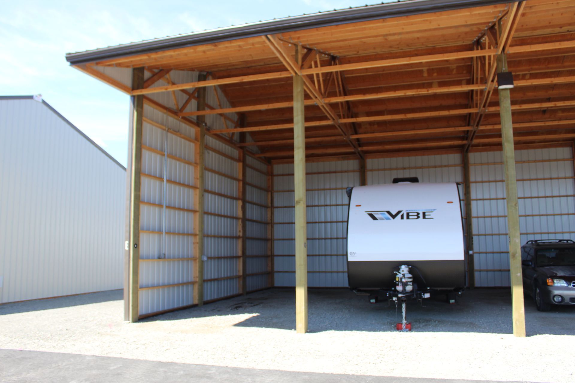 RV and truck parked under a wooden carport with corrugated metal siding.