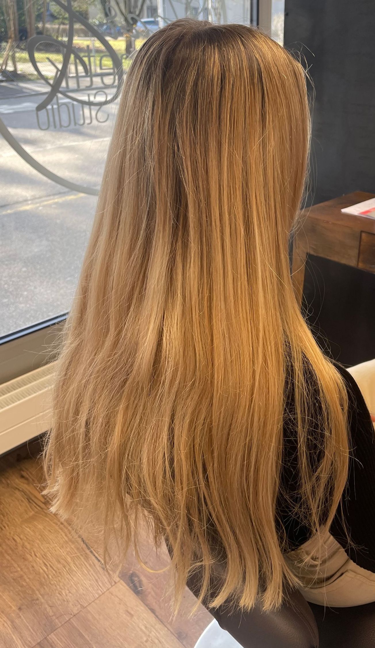 Frau mit langen, blonden Haaren sitzt am Fenster. Das Sonnenlicht wird von den Haaren reflektiert.