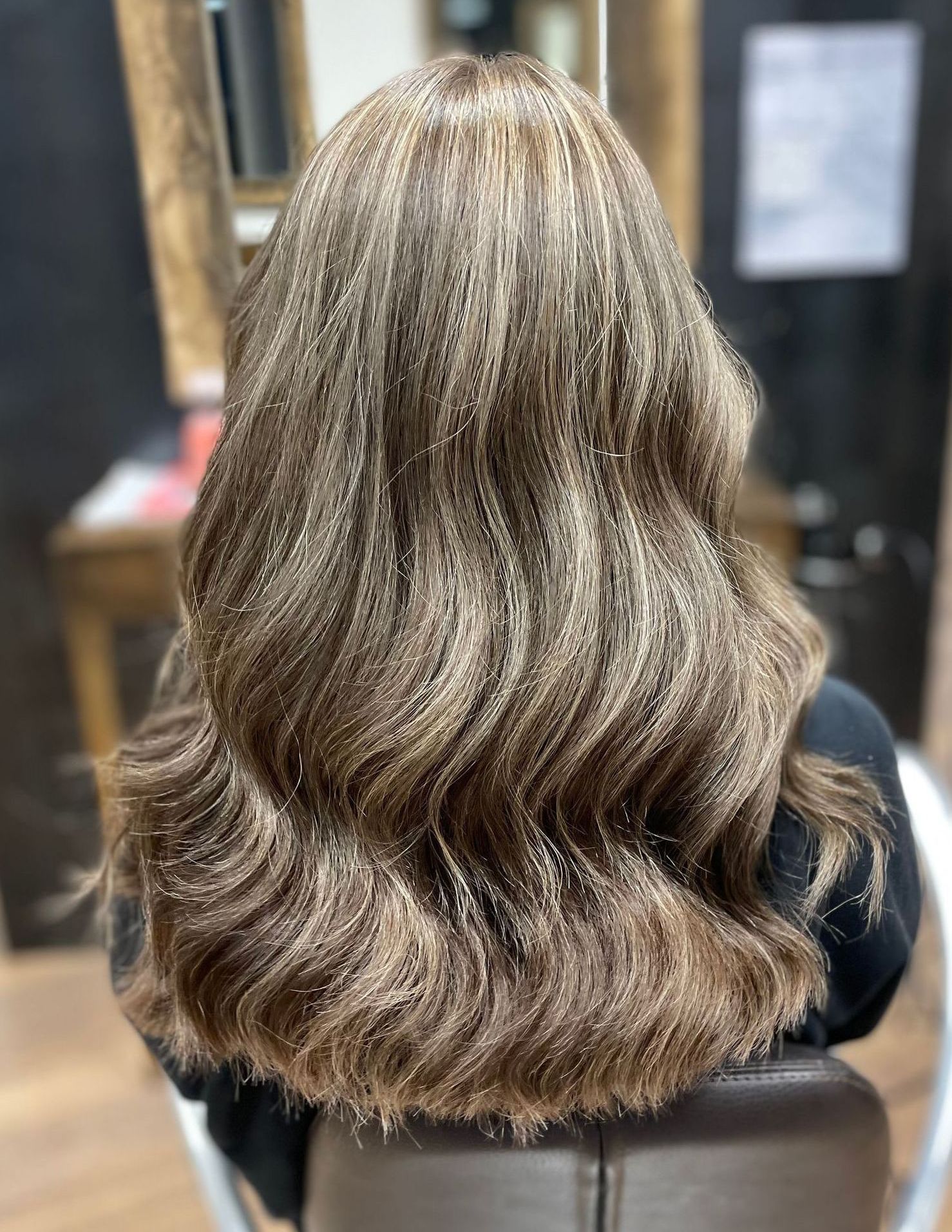Langes, welliges braunes Haar einer Frau mit Strähnchen, im Salon gestylt.