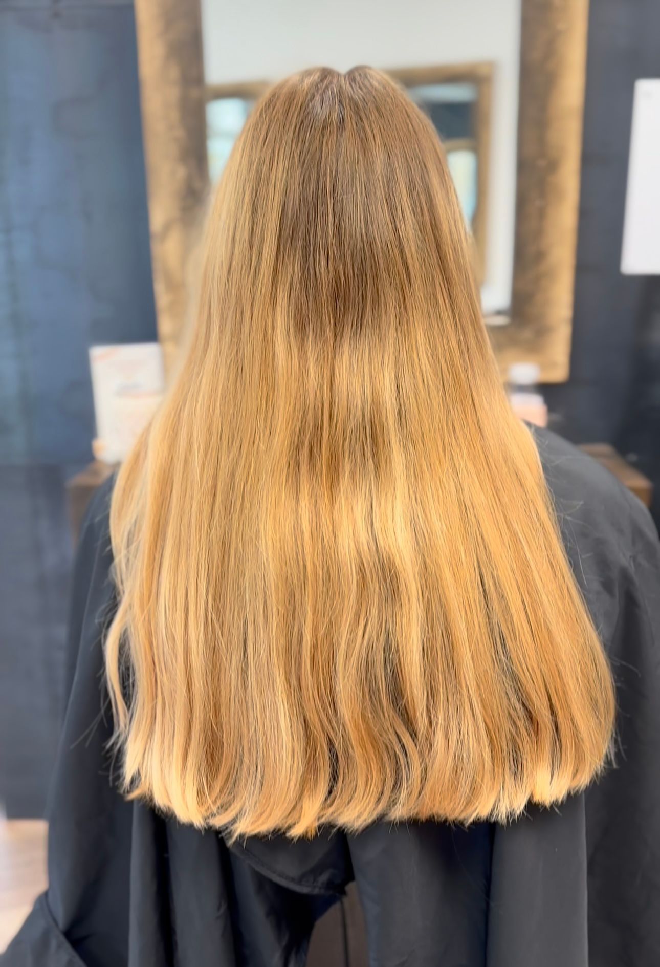 Das lange, gekräuselte, hellbraune Haar einer Frau vor einem goldenen Spiegelhintergrund und mit einem schwarzen Umhang.