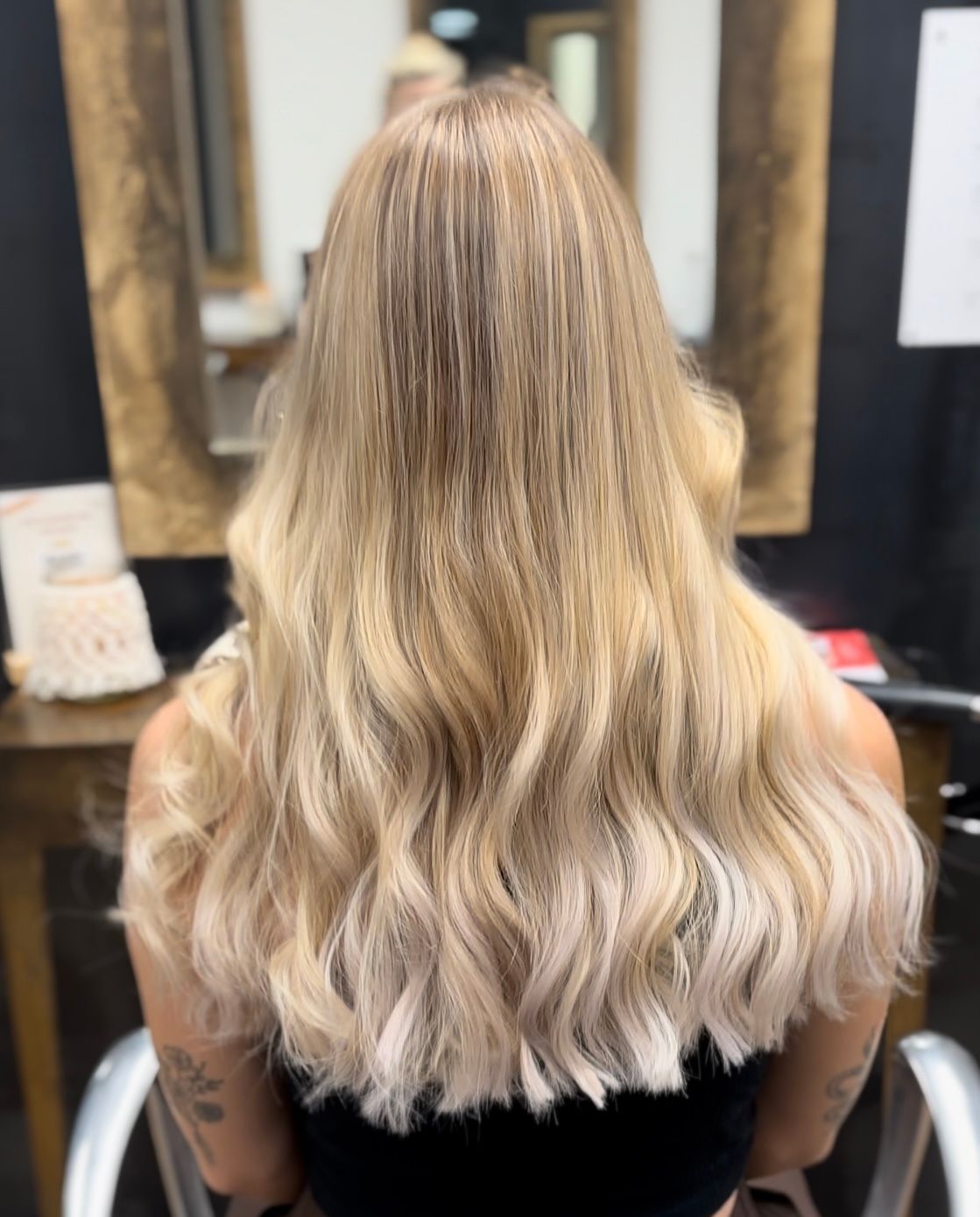 Frau mit langen, welligen, blonden Haaren, Rückansicht, gestylt in einem Salon.