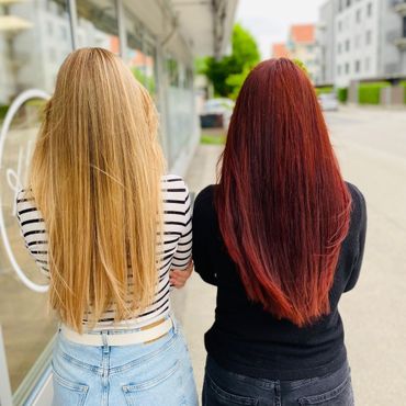 Frisch vom Coiffeur.
Zwei Frauen gehen auf einem Bürgersteig; eine mit blondem, gewelltem Haar, die andere mit rotem Haar.