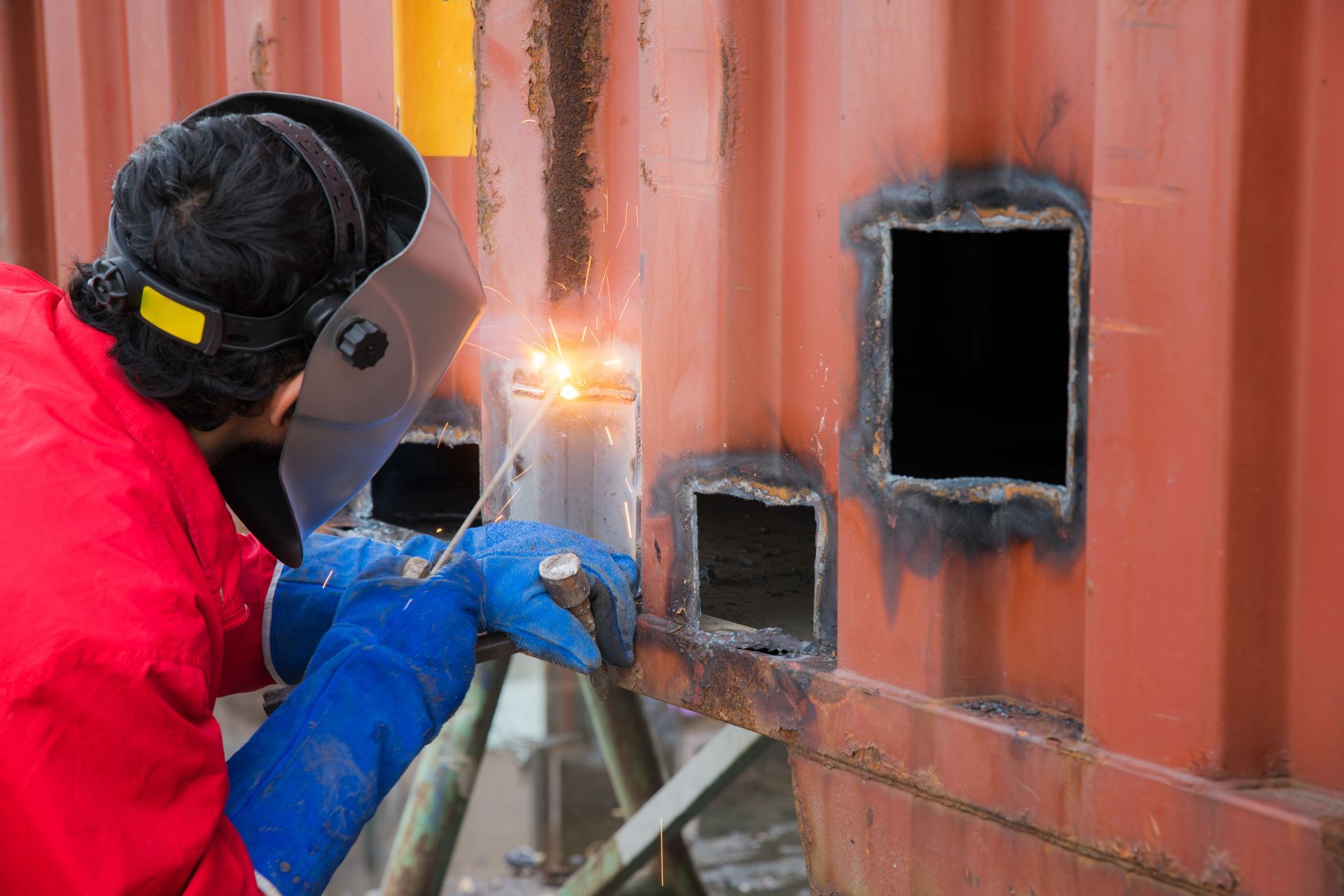 A man is welding a metal container with a welding mask on.
