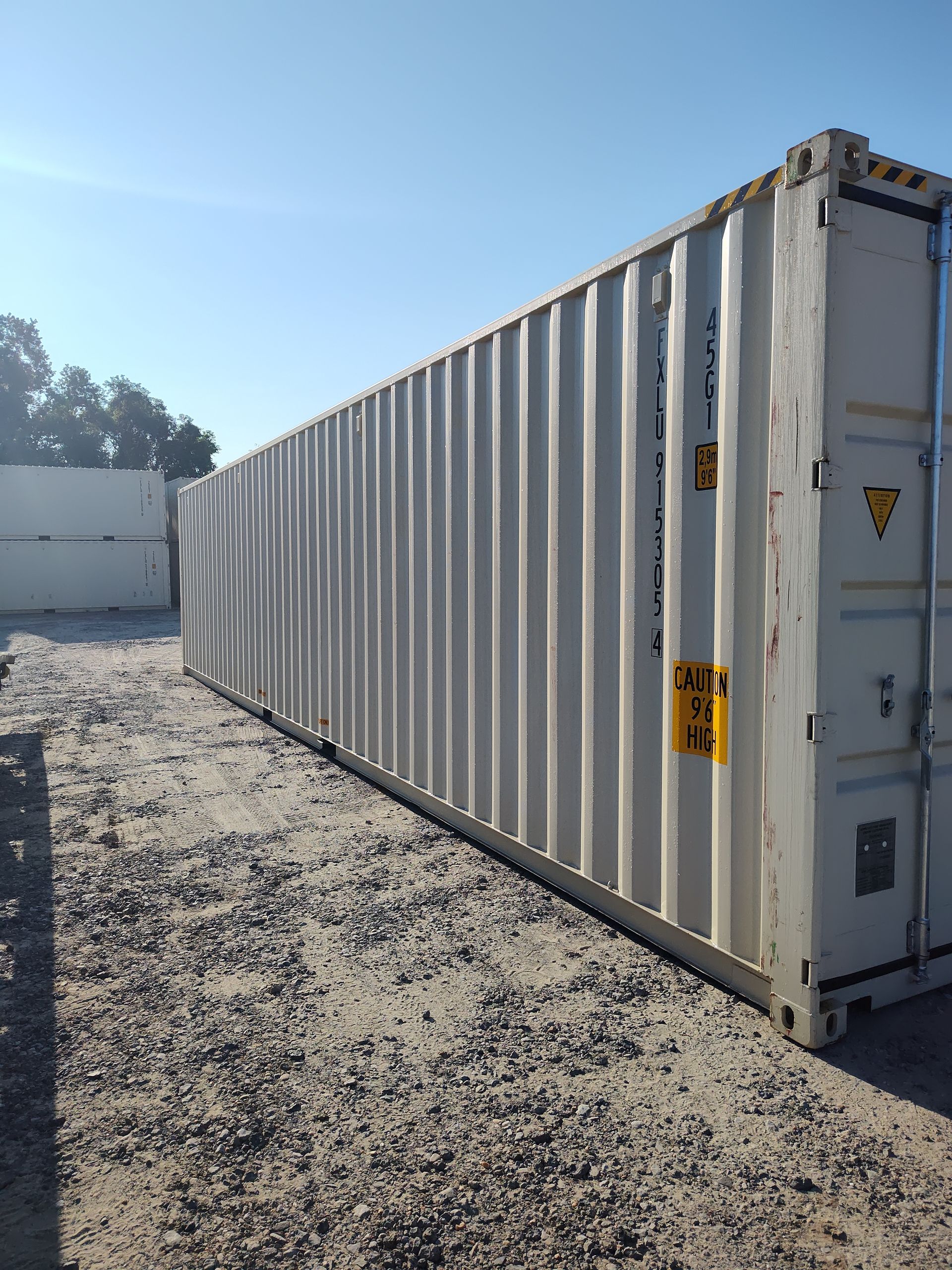 A semi truck is driving down a road next to a row of shipping containers.