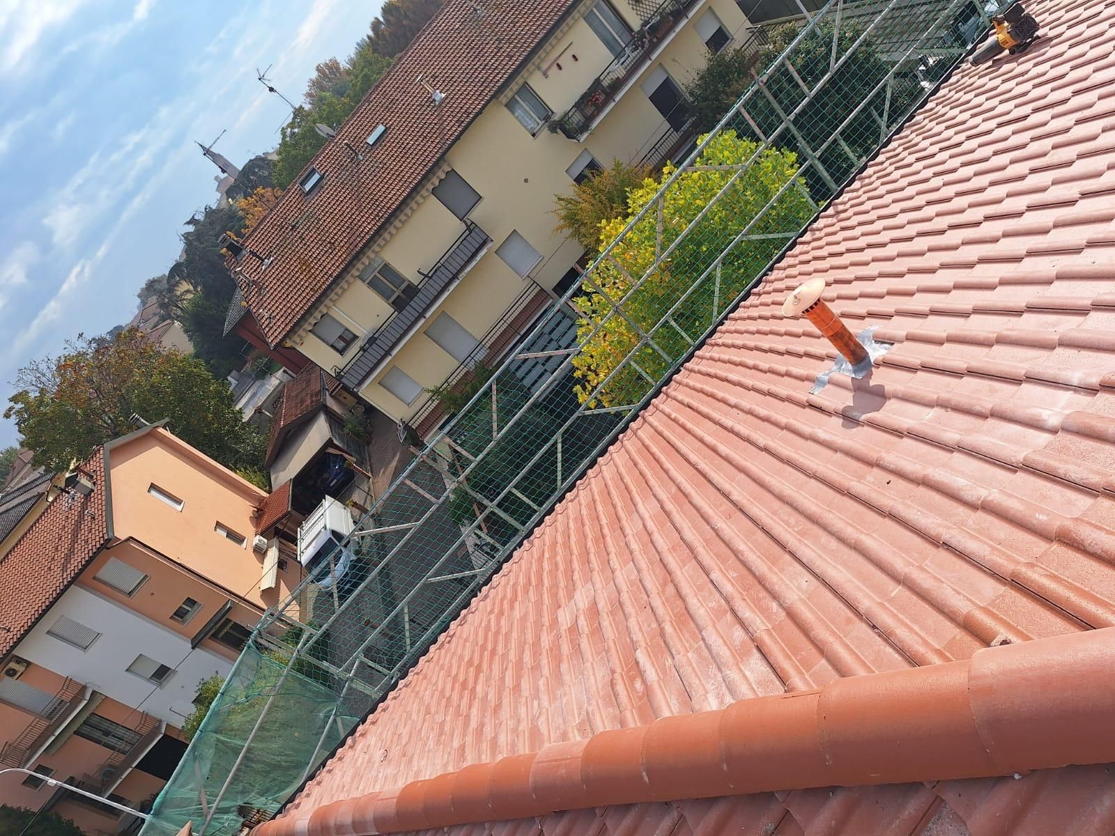 Tetto di tegole rosse con rete di sicurezza, edifici sullo sfondo, cielo azzurro.