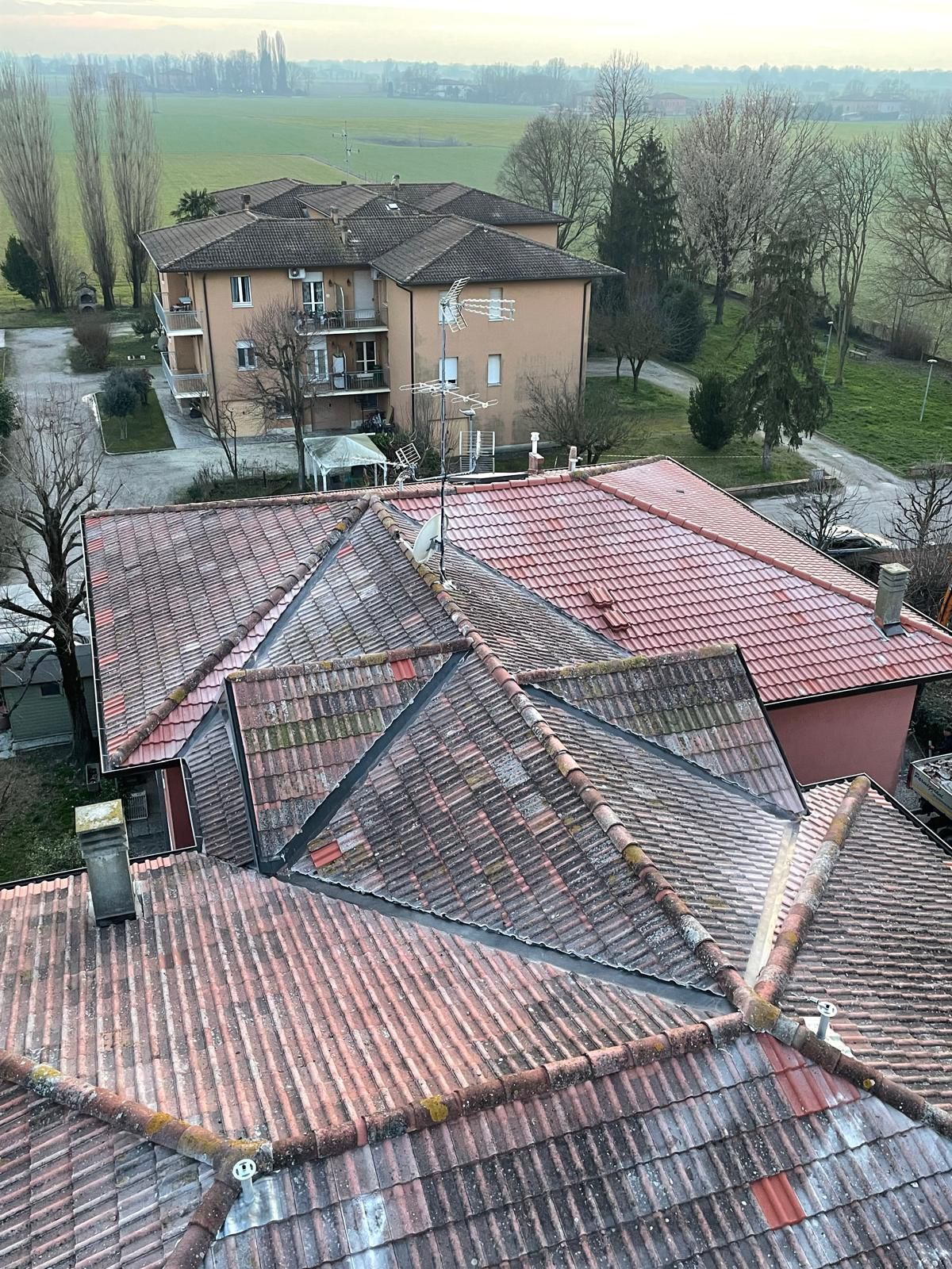 Tetti di edifici con tetti di tegole rosse, visti dall'alto, con un edificio più grande sullo sfondo e un campo.
