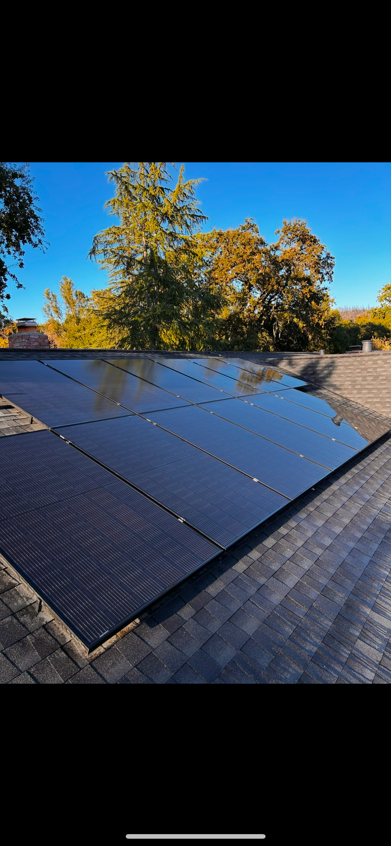 Solar panels on a roof, blue sky and trees in background.