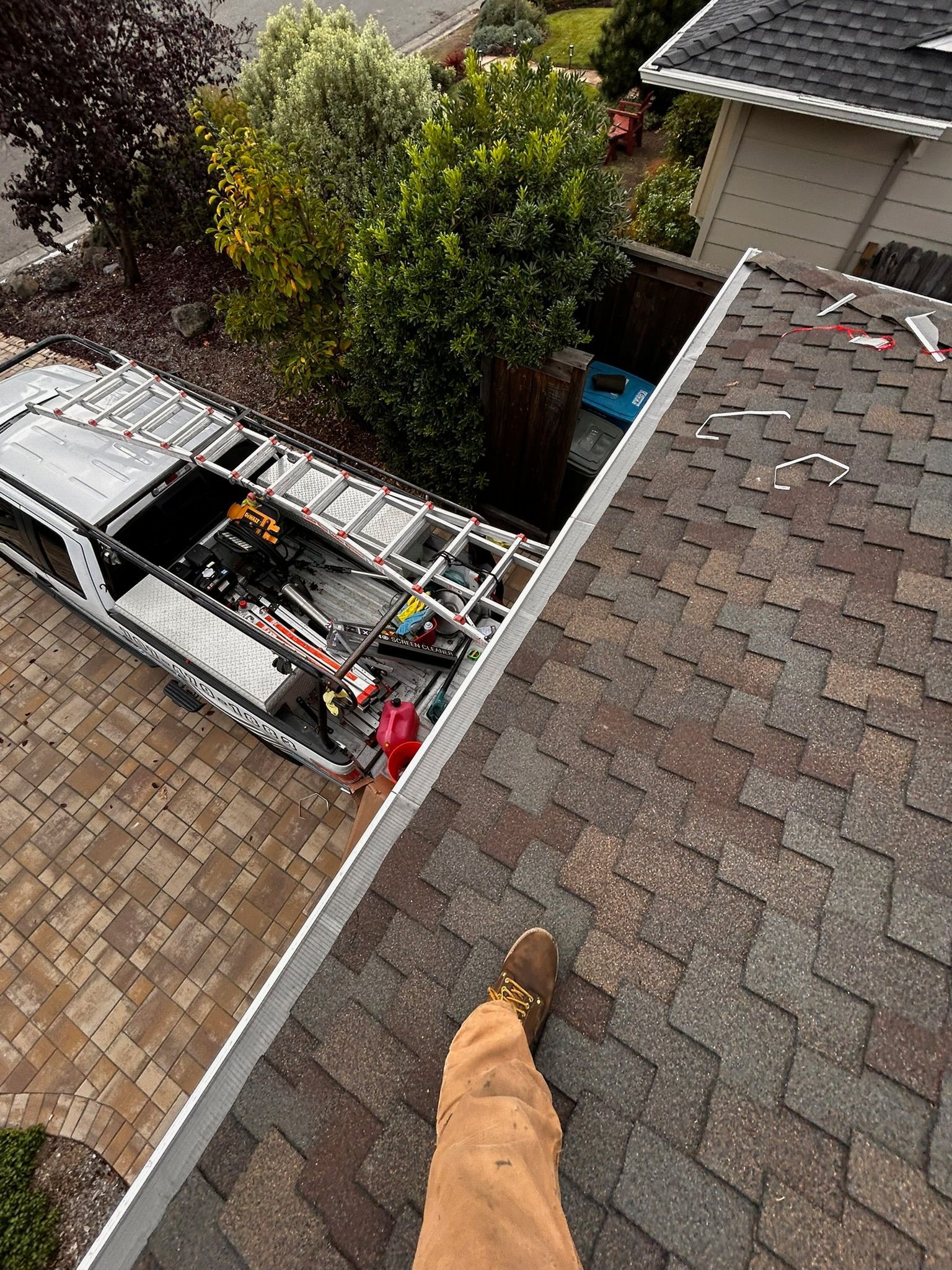 Person on roof near gutter, service truck below with ladder and tools.